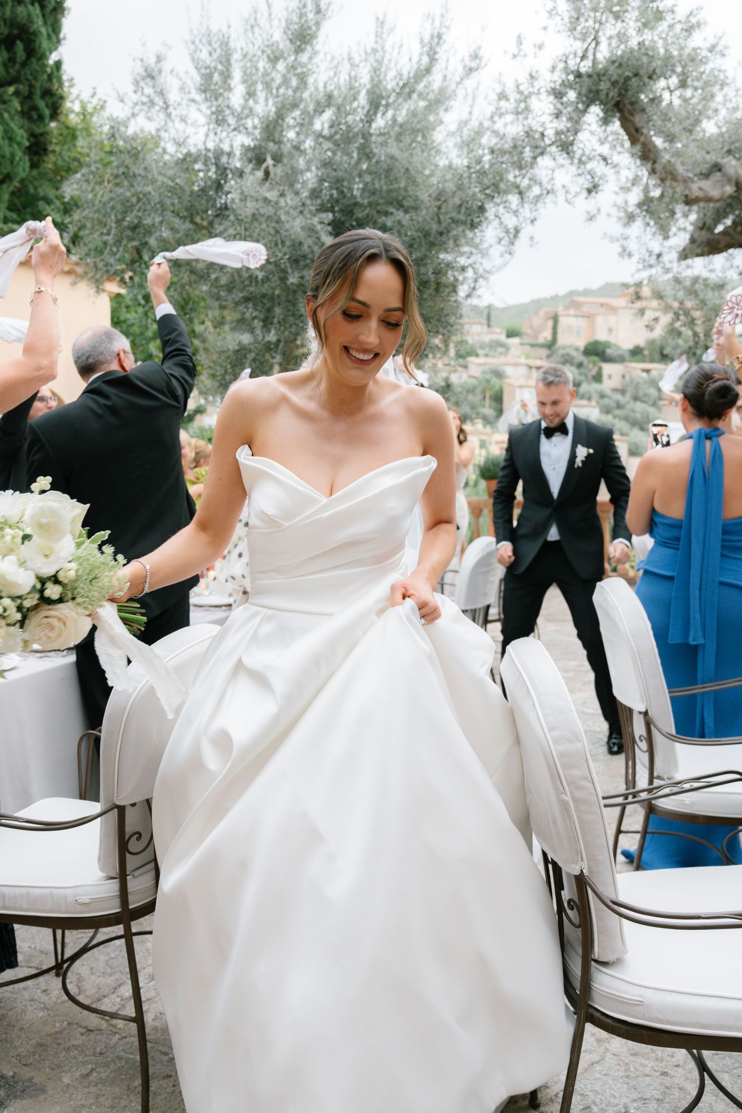 Wedding celebration moments captured on an outdoor patio with white chairs and olive trees.