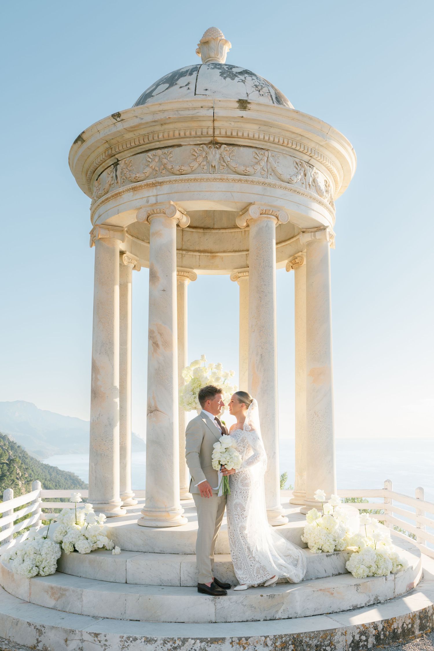 Elegant white stone gazebo decorated with floral arrangements for a wedding ceremony.
