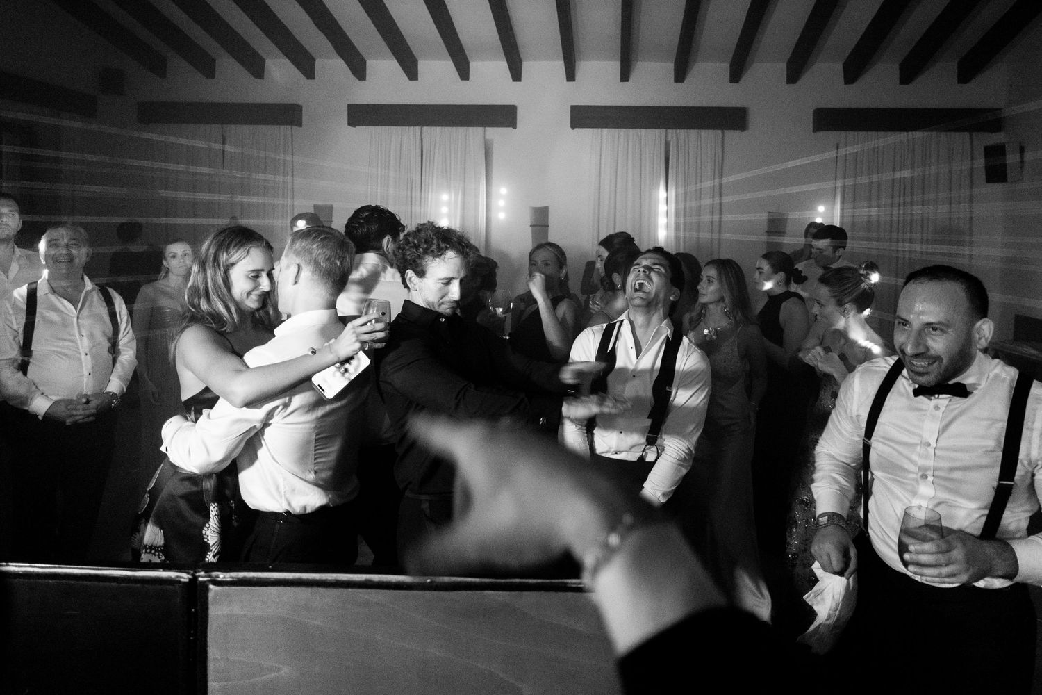 Silhouettes of wedding guests dancing and celebrating at a reception under dramatic lighting.