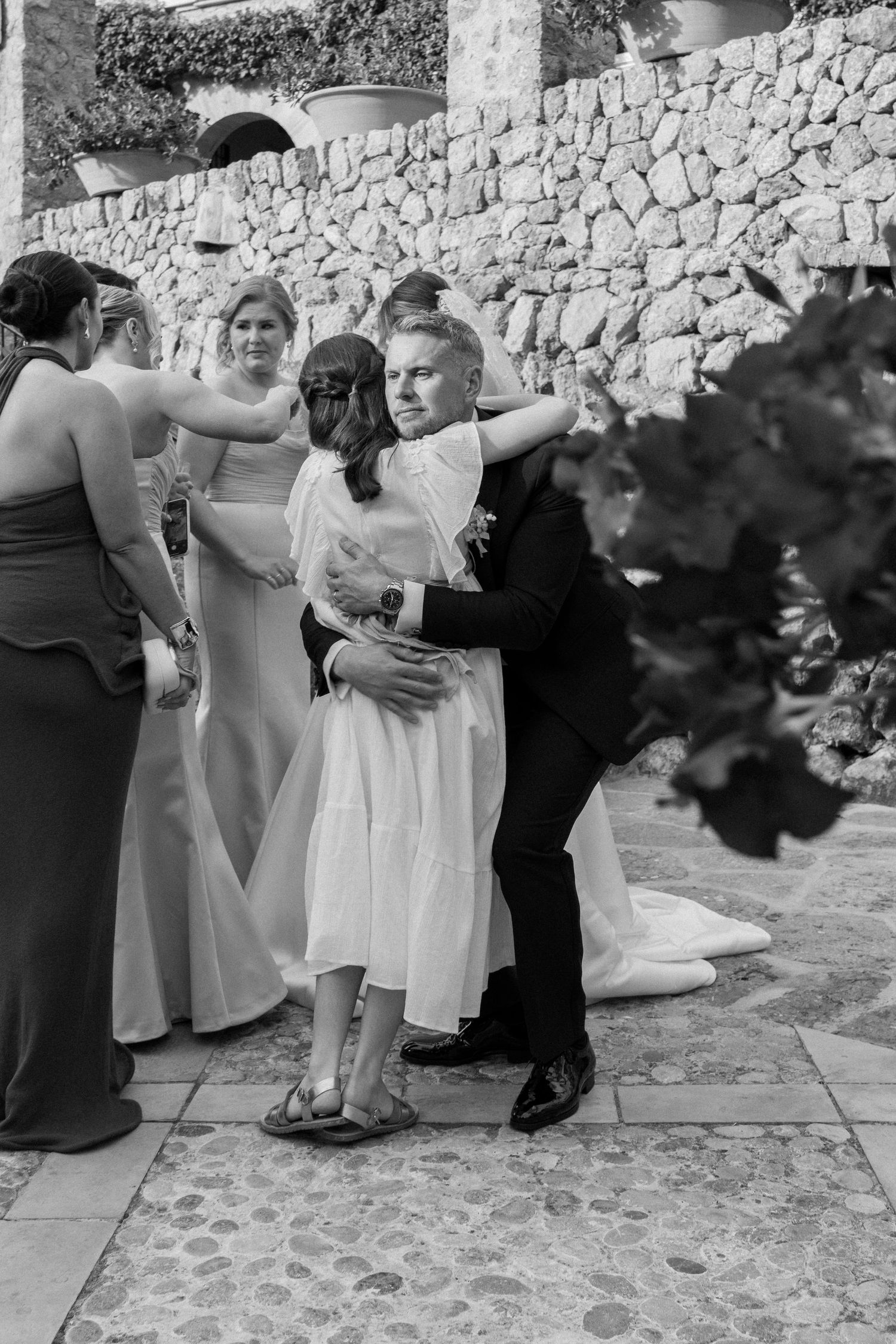 Wedding party members embrace during emotional moments at an outdoor reception.