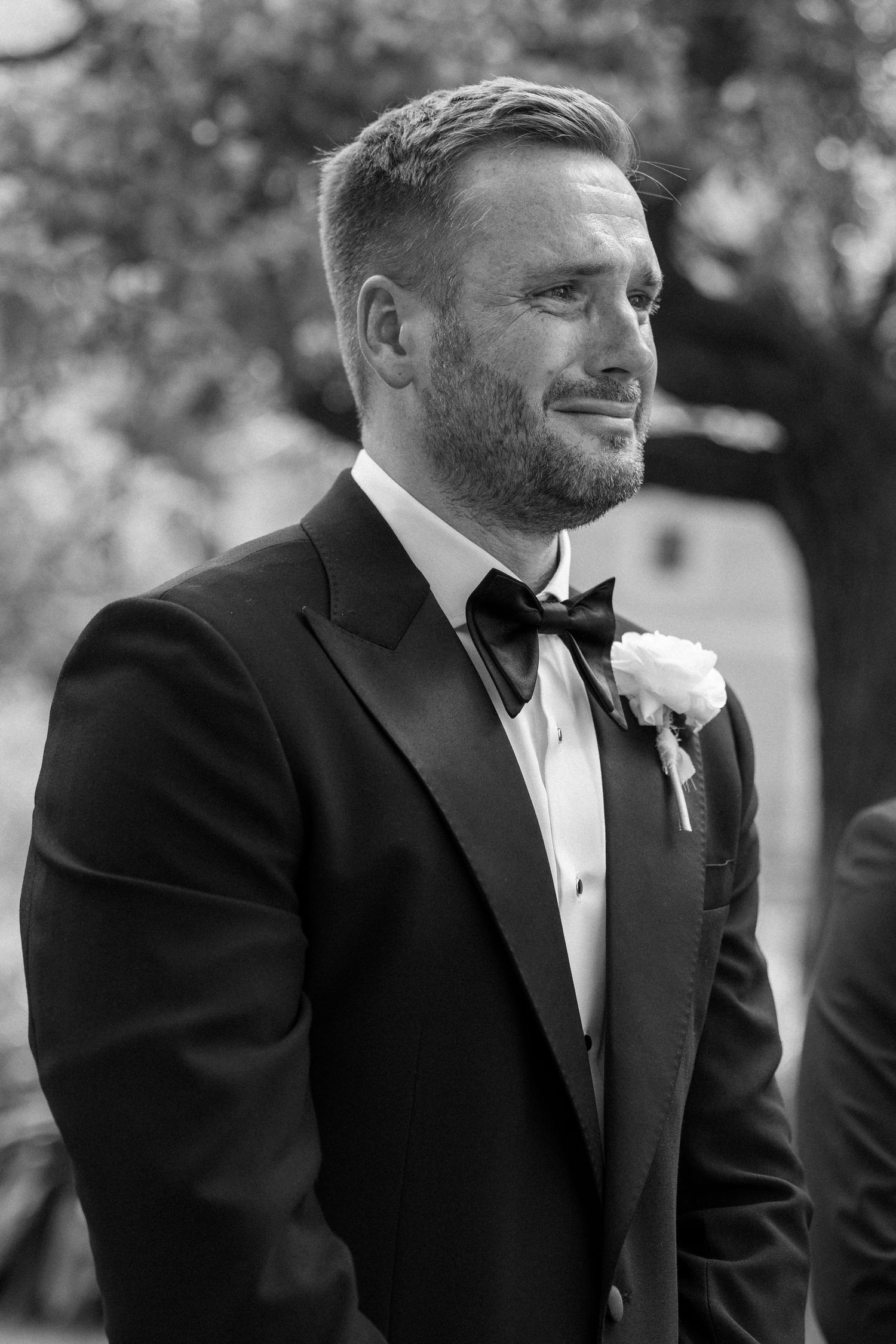 Black and white portrait of groomsmen in tuxedos at outdoor wedding.