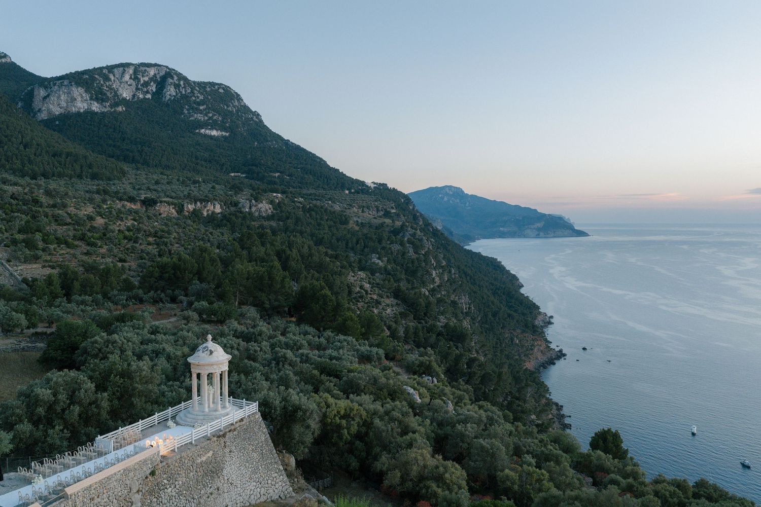 Scenic mountain coastline with classical architecture and blue Mediterranean waters at sunset.