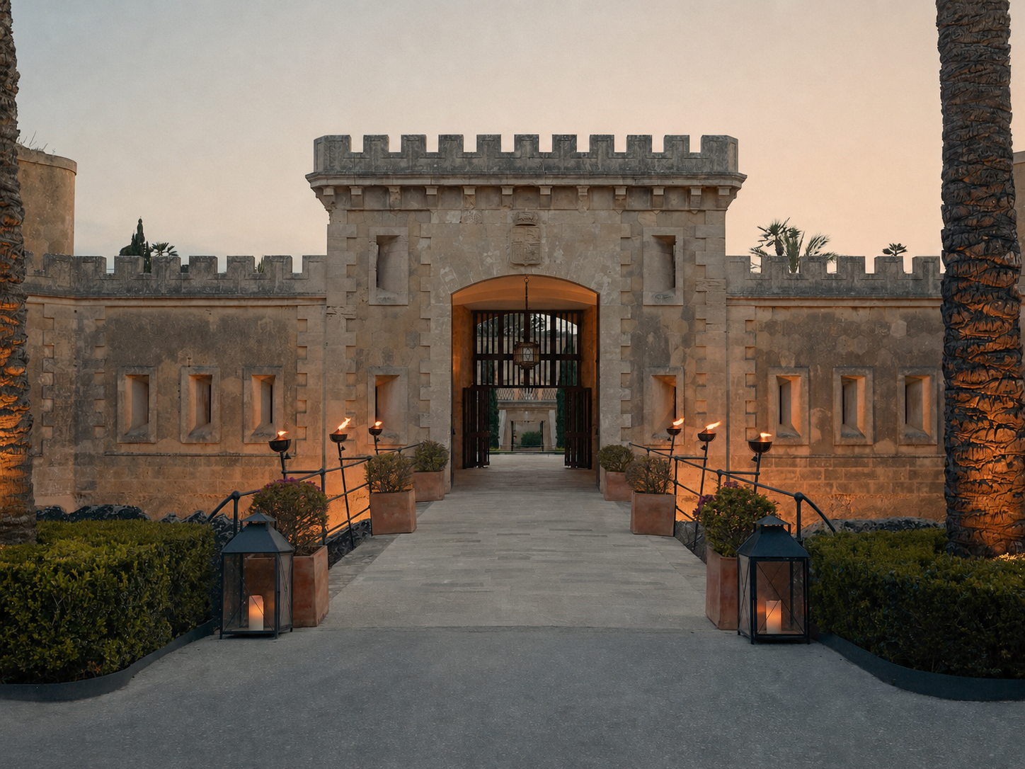 Cap Rocat stone entrance with arched gateway, lanterns, and battlements at dusk, evoking a grand historic estate.