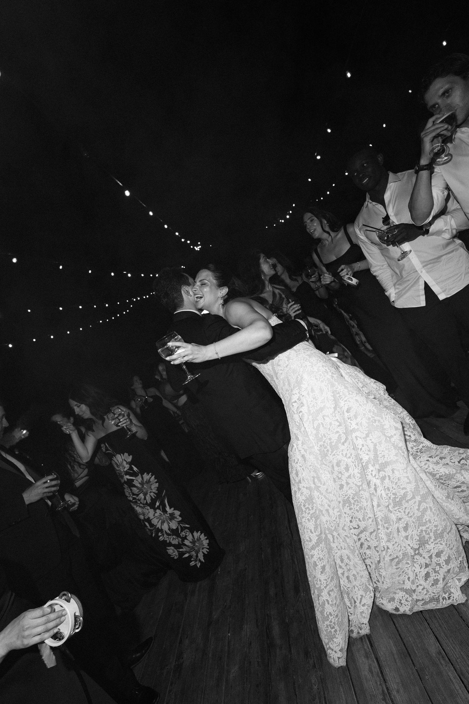 Black and white photo of bride and groom sharing first dance at wedding reception with guests watching.