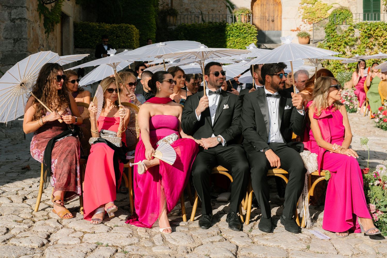 Wedding party in bright pink dresses and black tuxedos seated on stone steps.