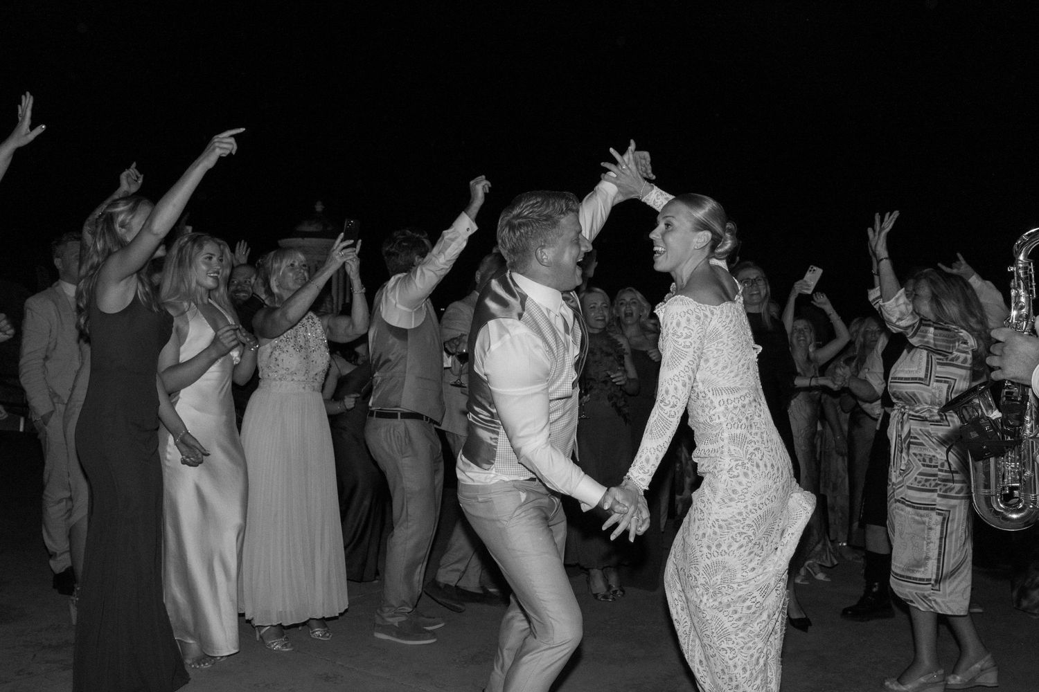 Party guests dancing and celebrating on a dark dance floor with festive lighting.