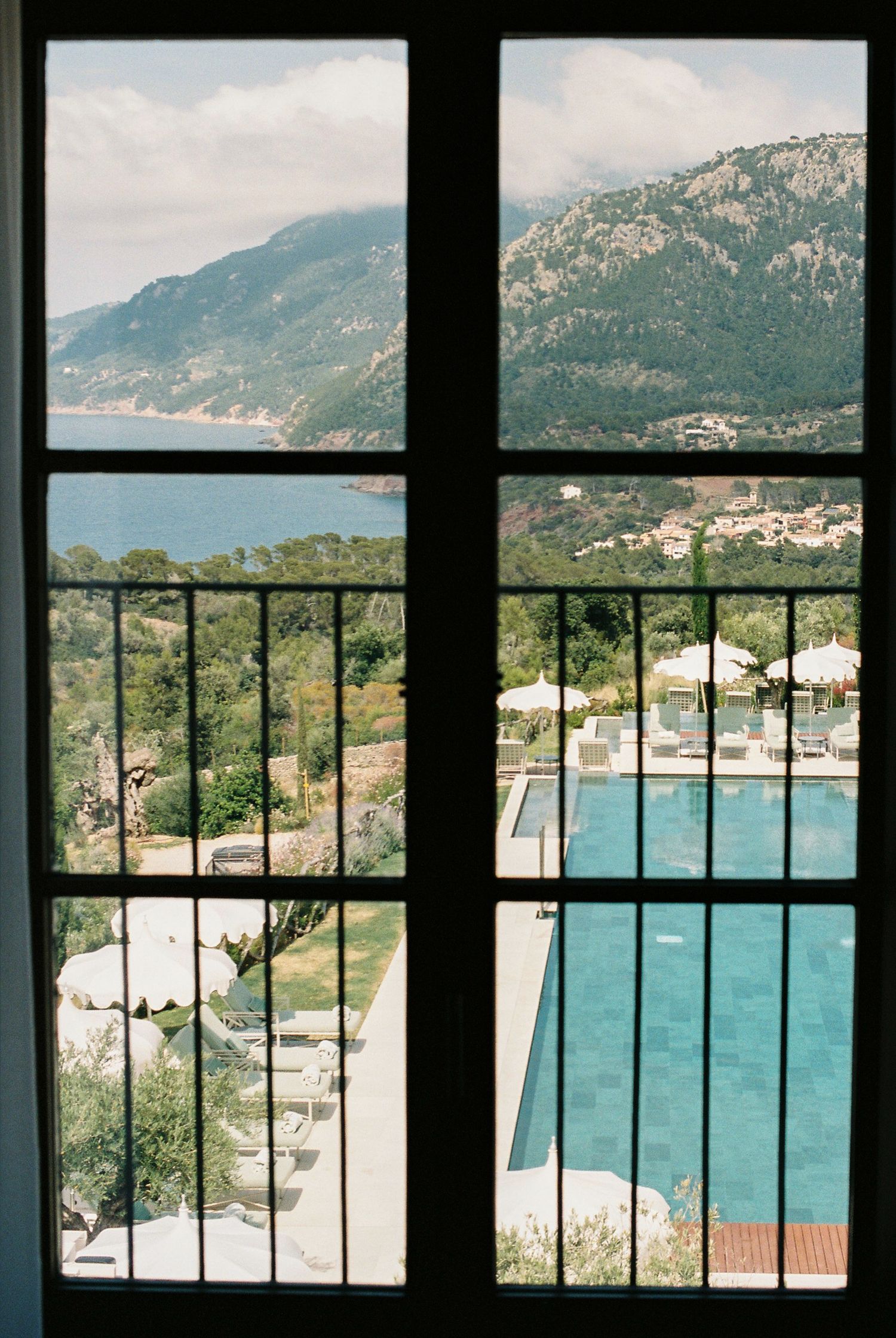 Panoramic mountain view through large window frames showcasing a turquoise pool below.