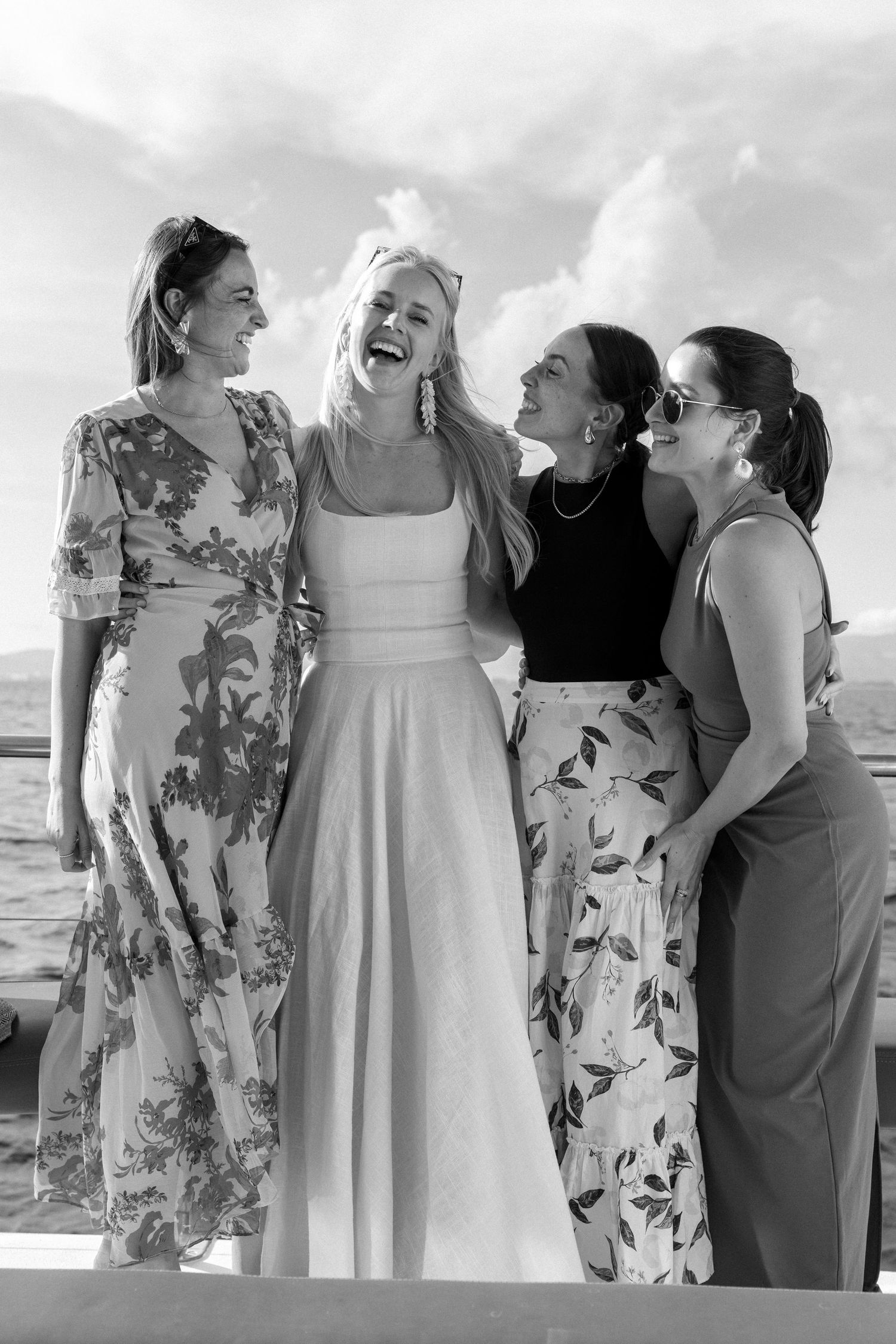 A group wearing floral dresses and formal attire poses together by the ocean.