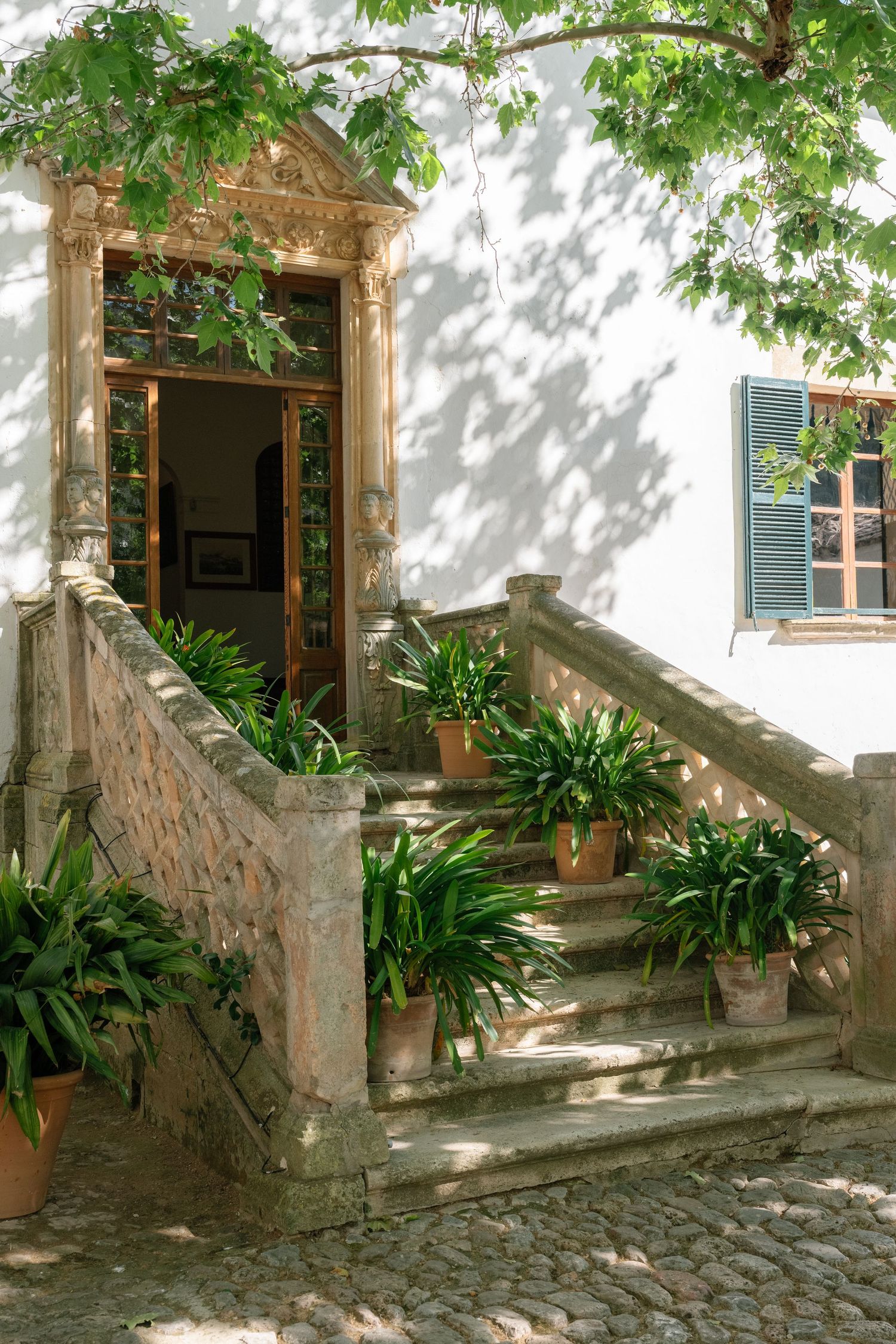 Stone staircase with terracotta potted plants leads to ornate doorway of historic white Mediterranean villa.