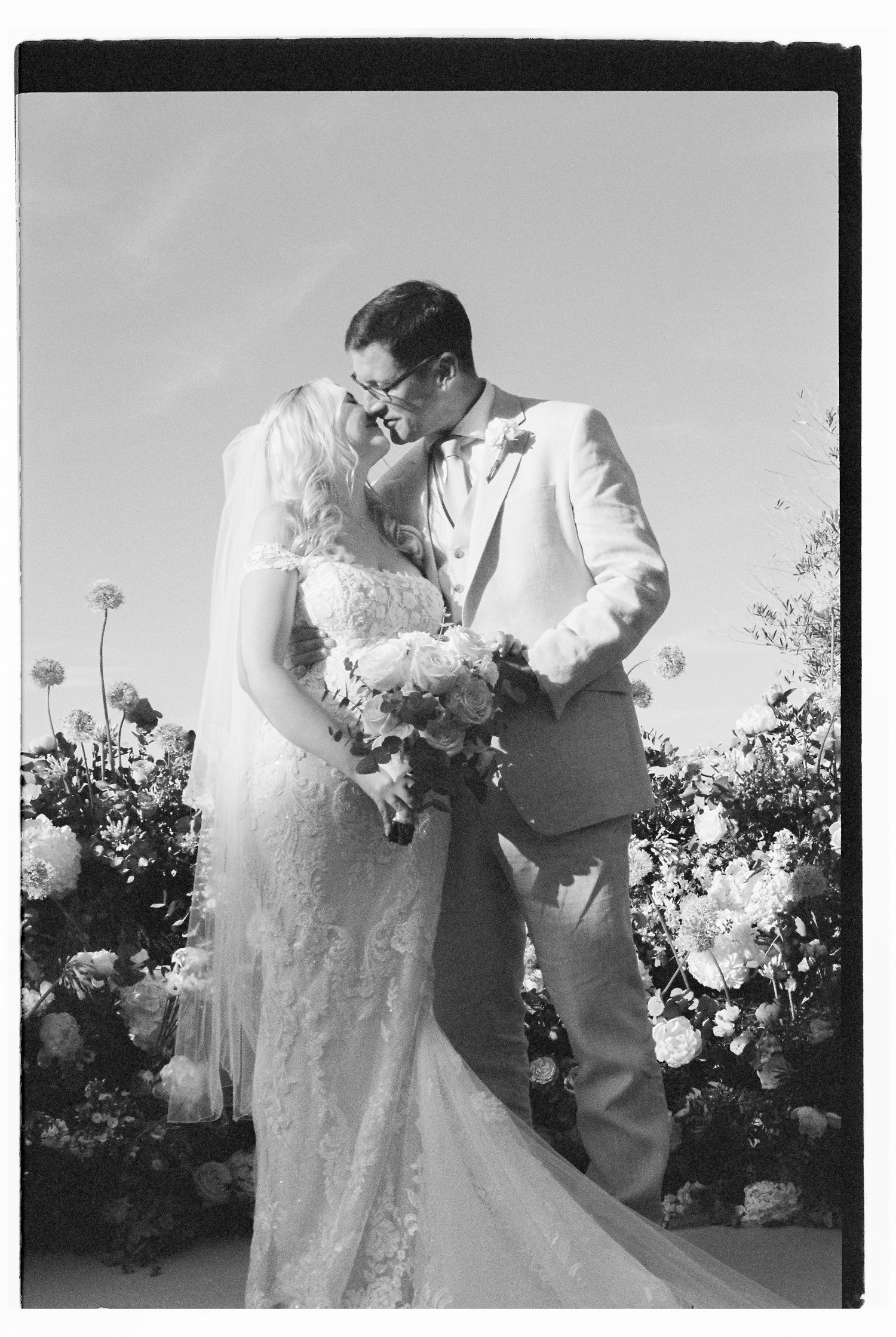 Romantic black and white wedding photo of couple embracing outdoors.