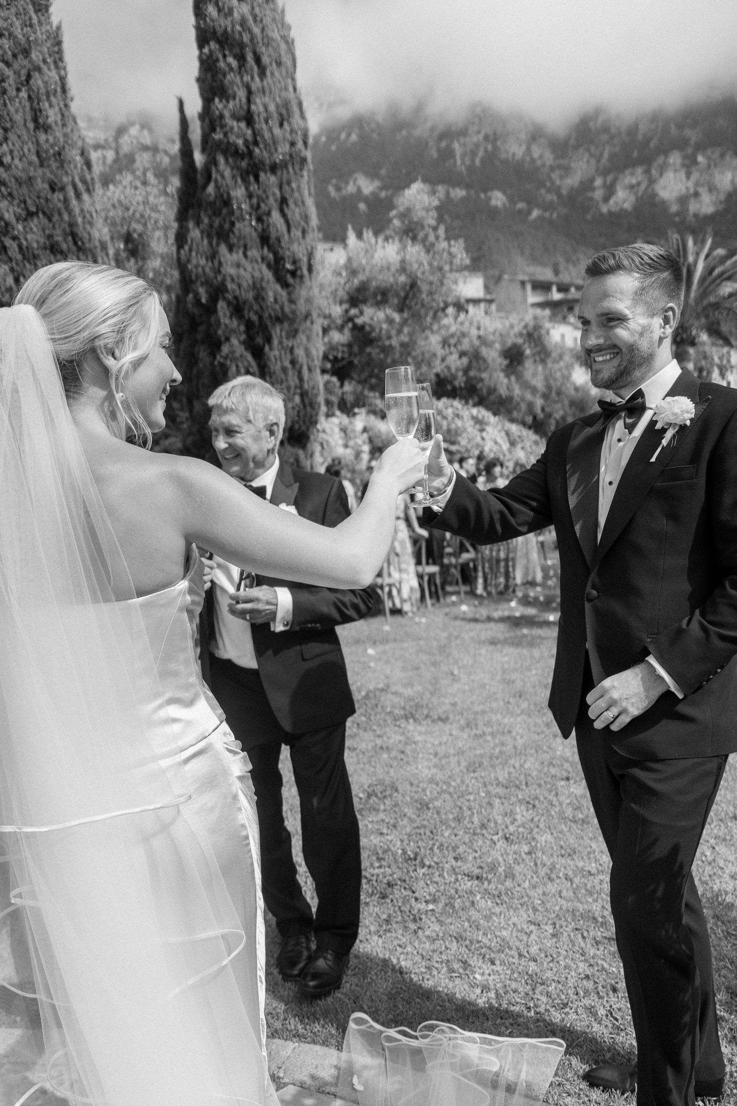 Black and white candid moment of couple toasting during outdoor wedding celebration.