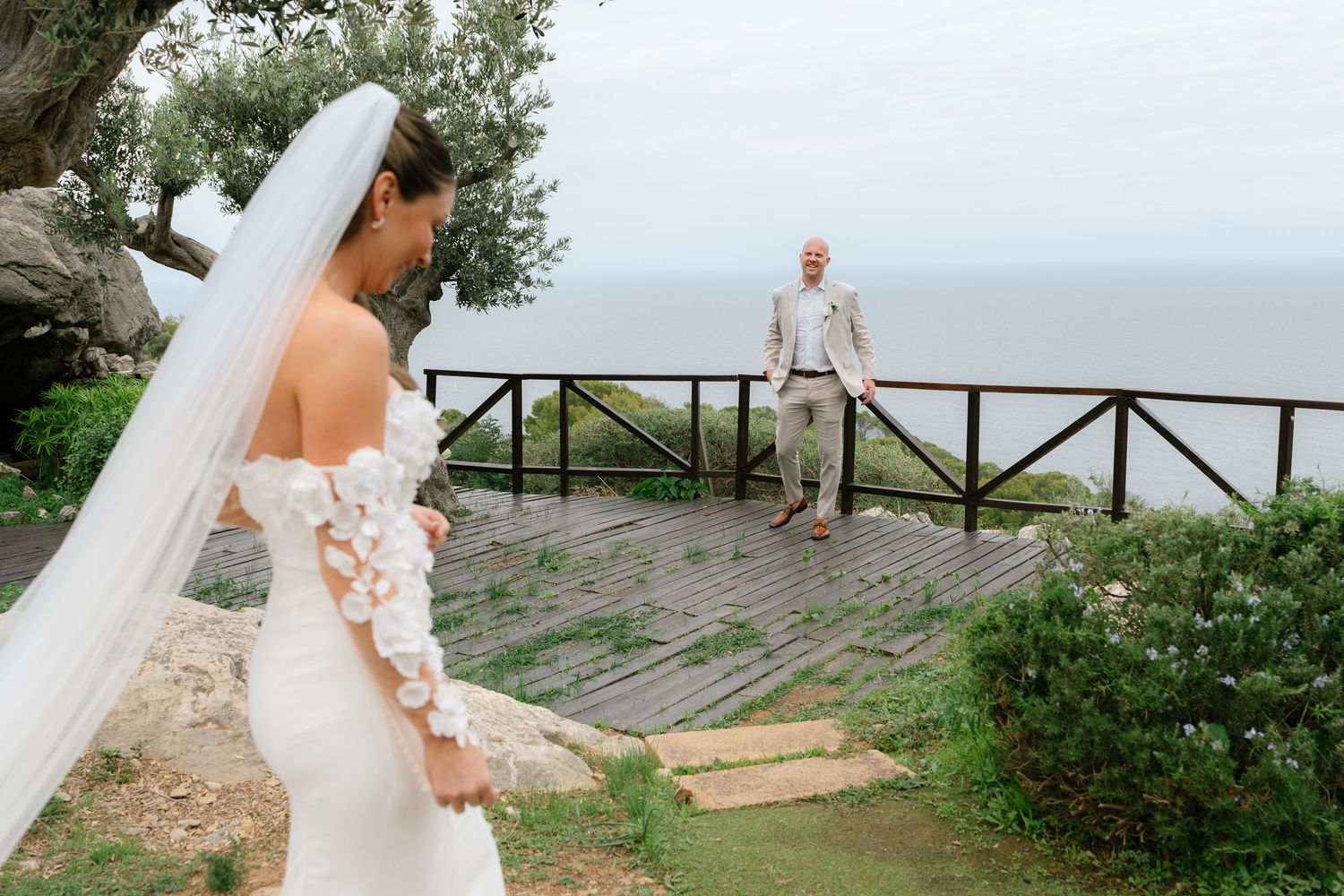 A wedding couple embraces on a scenic coastal overlook with mountains and ocean in the background.