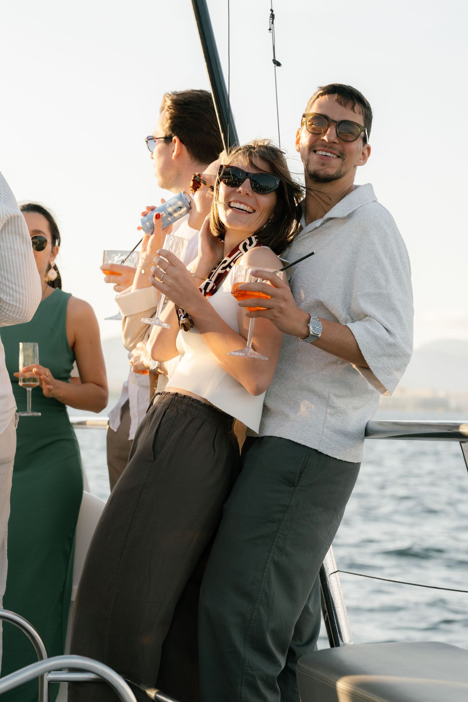 Party guests in formal attire socialize and drink on a boat deck with ocean views.