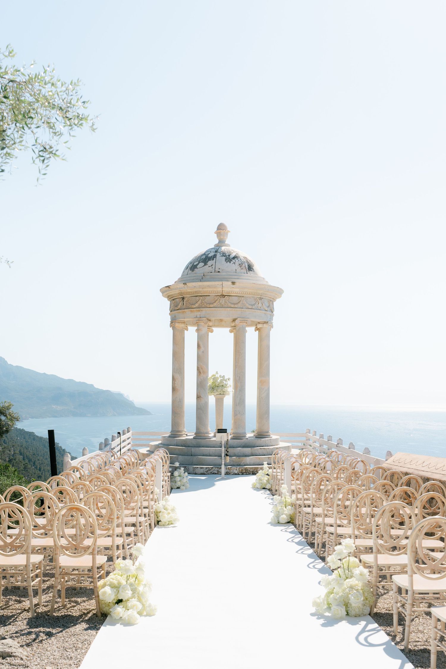 Elegant outdoor wedding ceremony setup with white chairs and a classical stone gazebo overlooking a scenic mountain view.