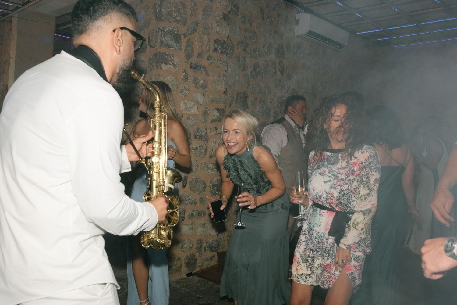 Musicians performing at an indoor party with guests dancing in the background.