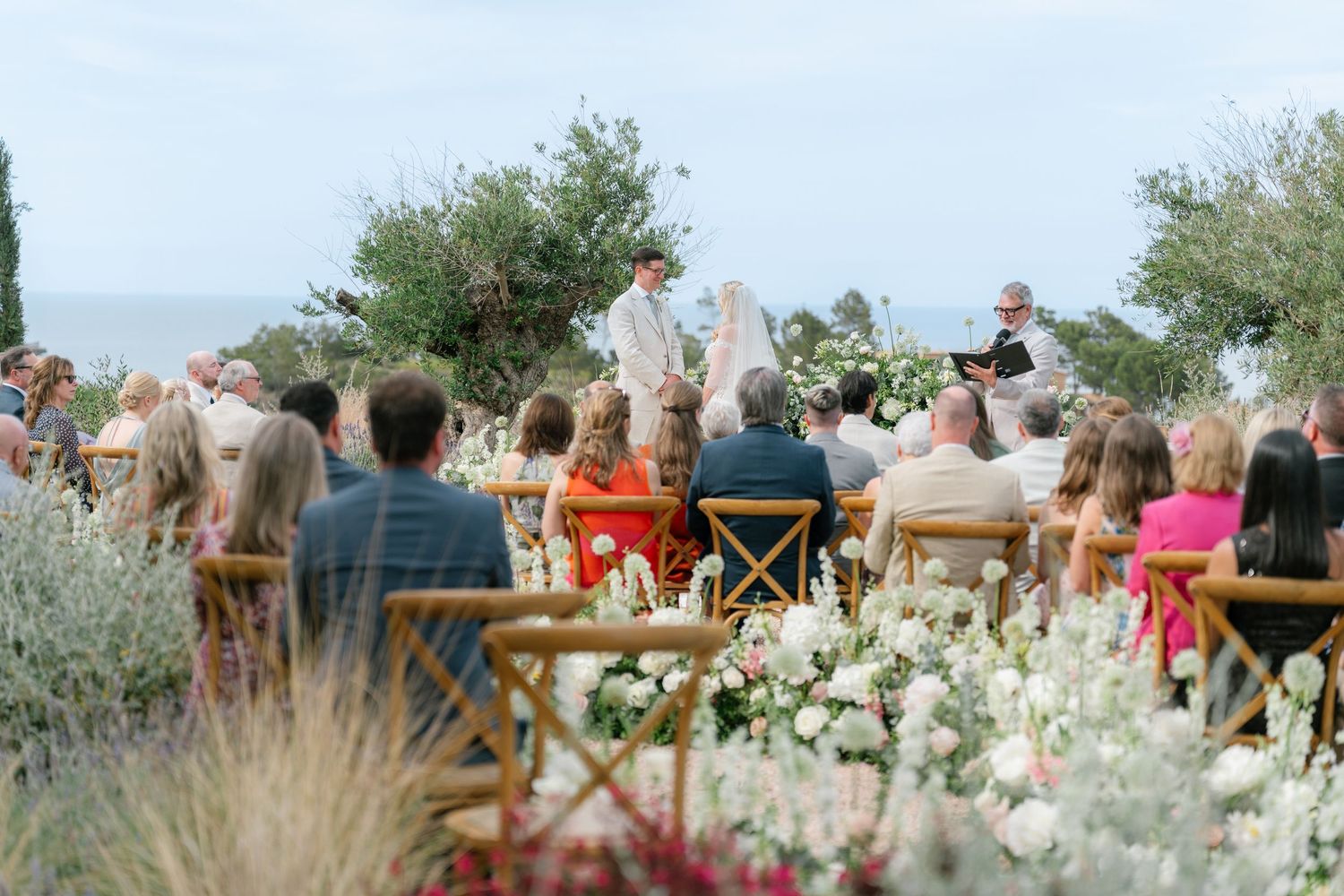 Wedding guests seated outdoors at a scenic mountain venue with white floral arrangements.