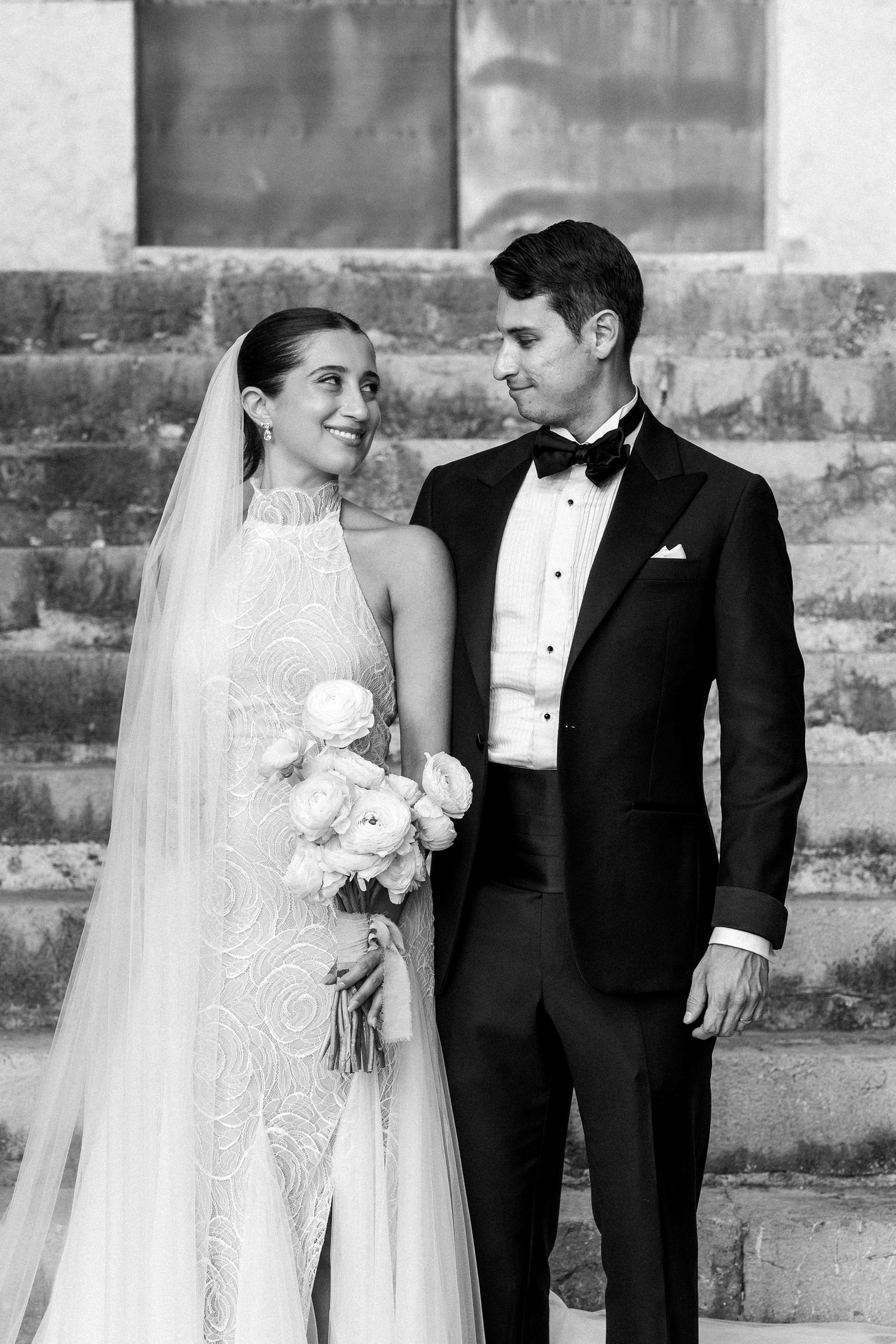 A romantic black and white wedding portrait of a couple standing on stone steps.