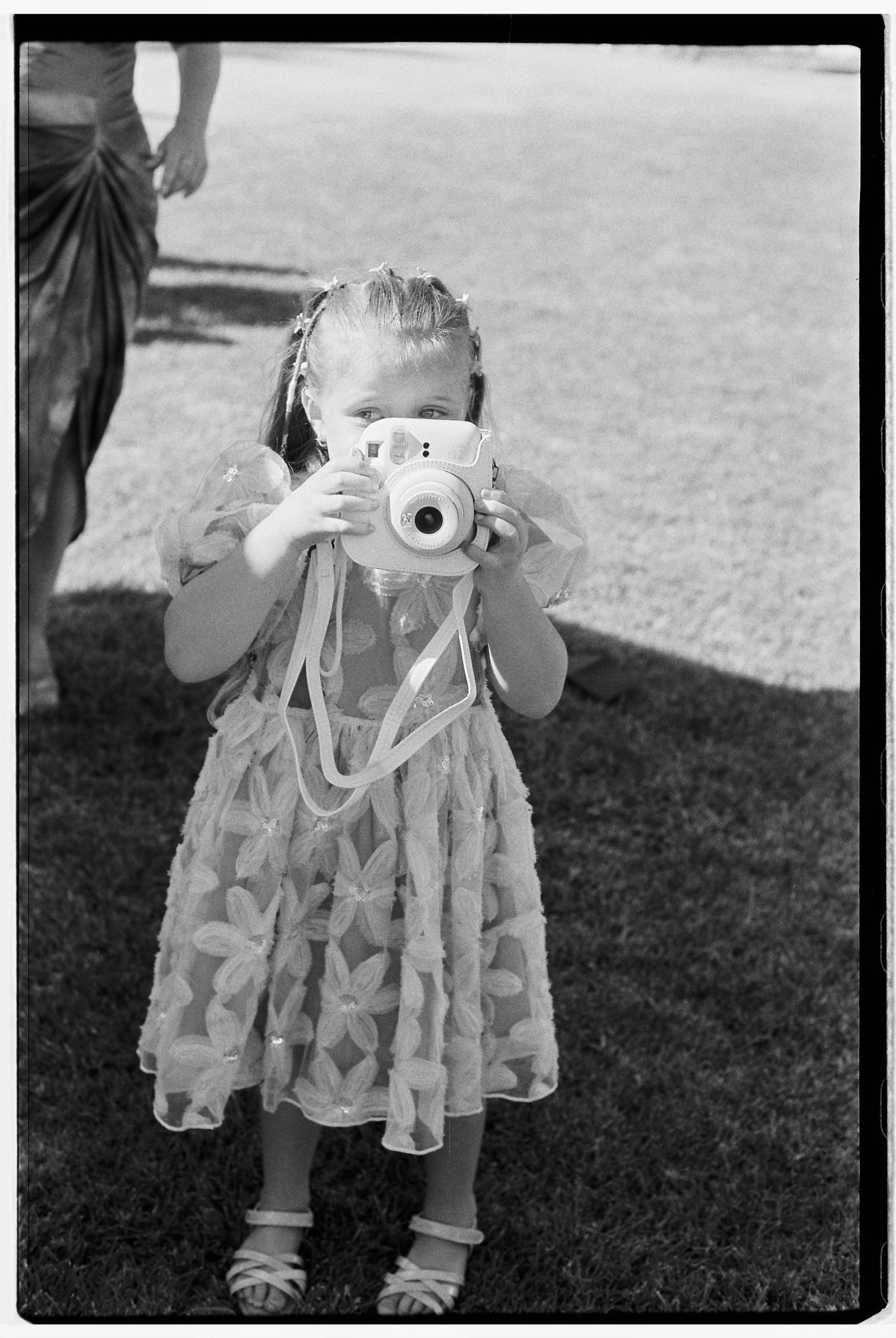 Young child in a frilly dress taking pictures with a camera.