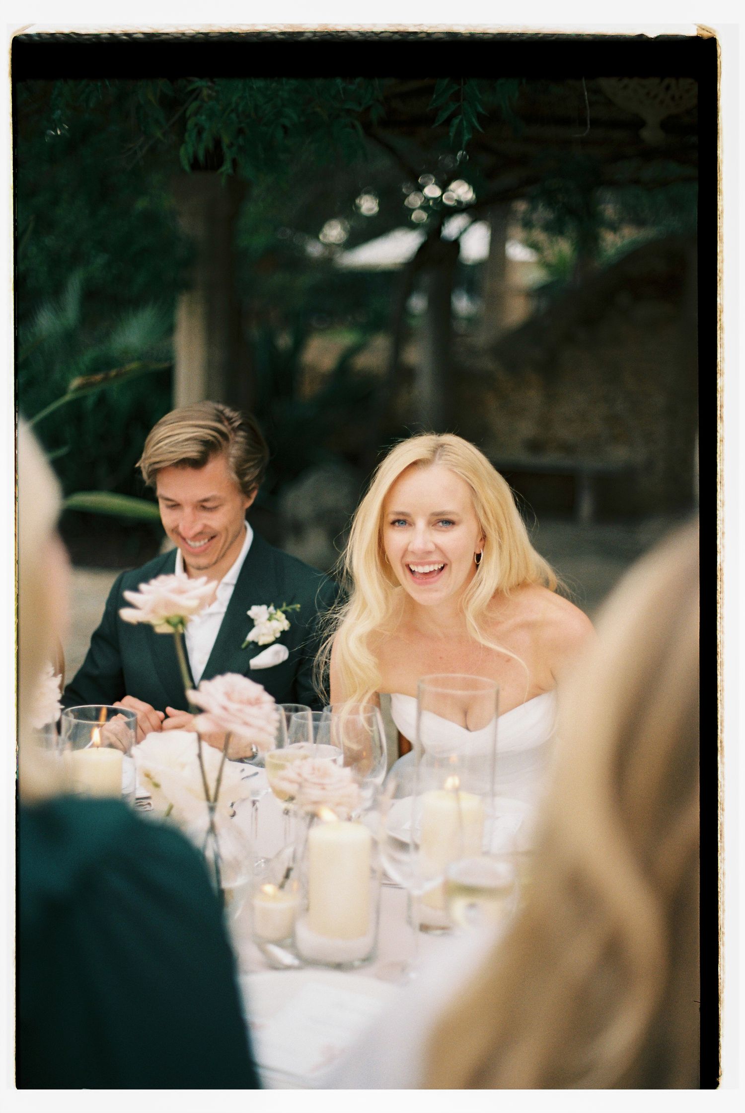 Wedding couple sharing laughter at an outdoor reception dinner table.