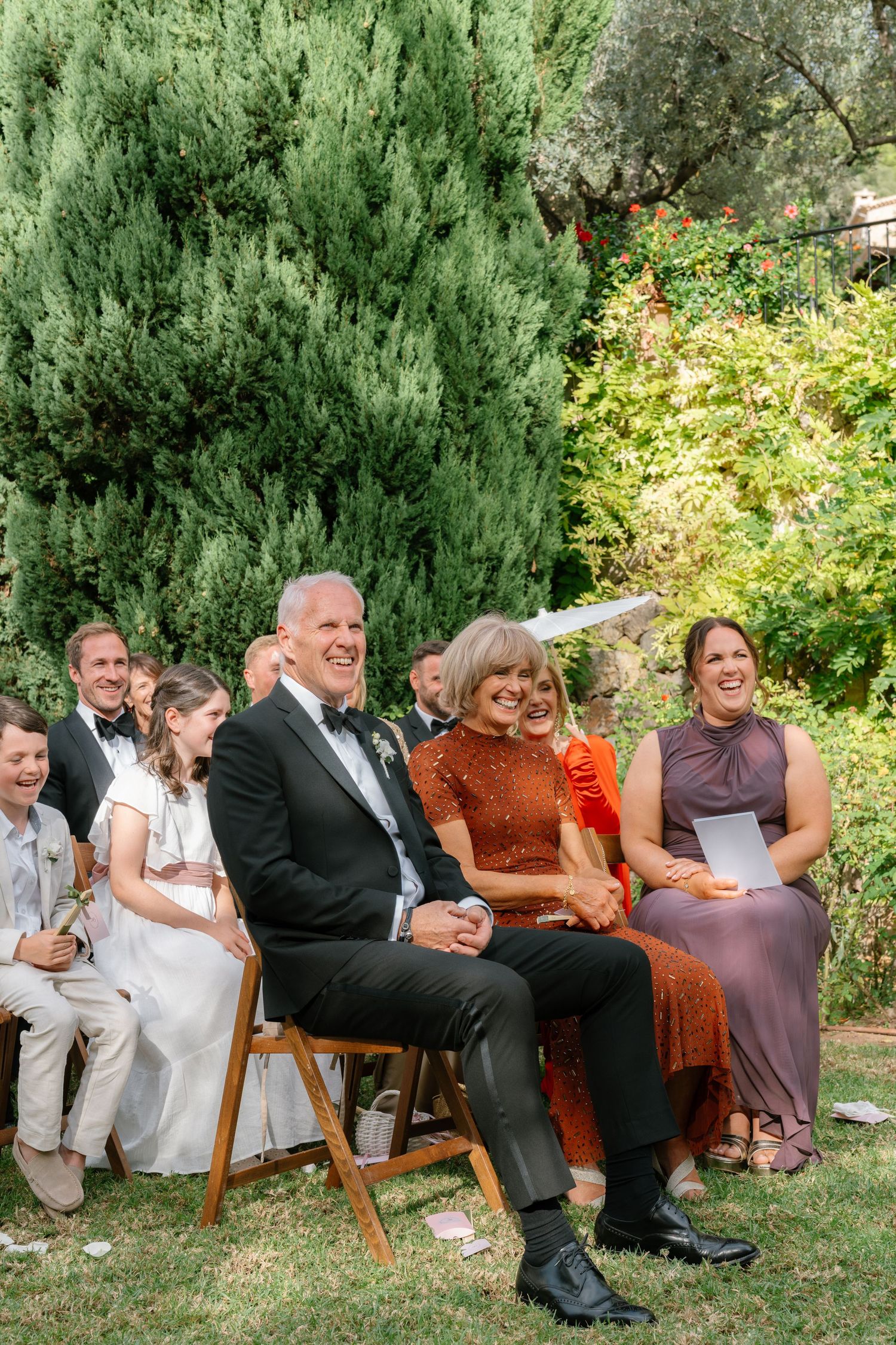Wedding guests seated on vintage furniture outdoors during an elegant garden ceremony.