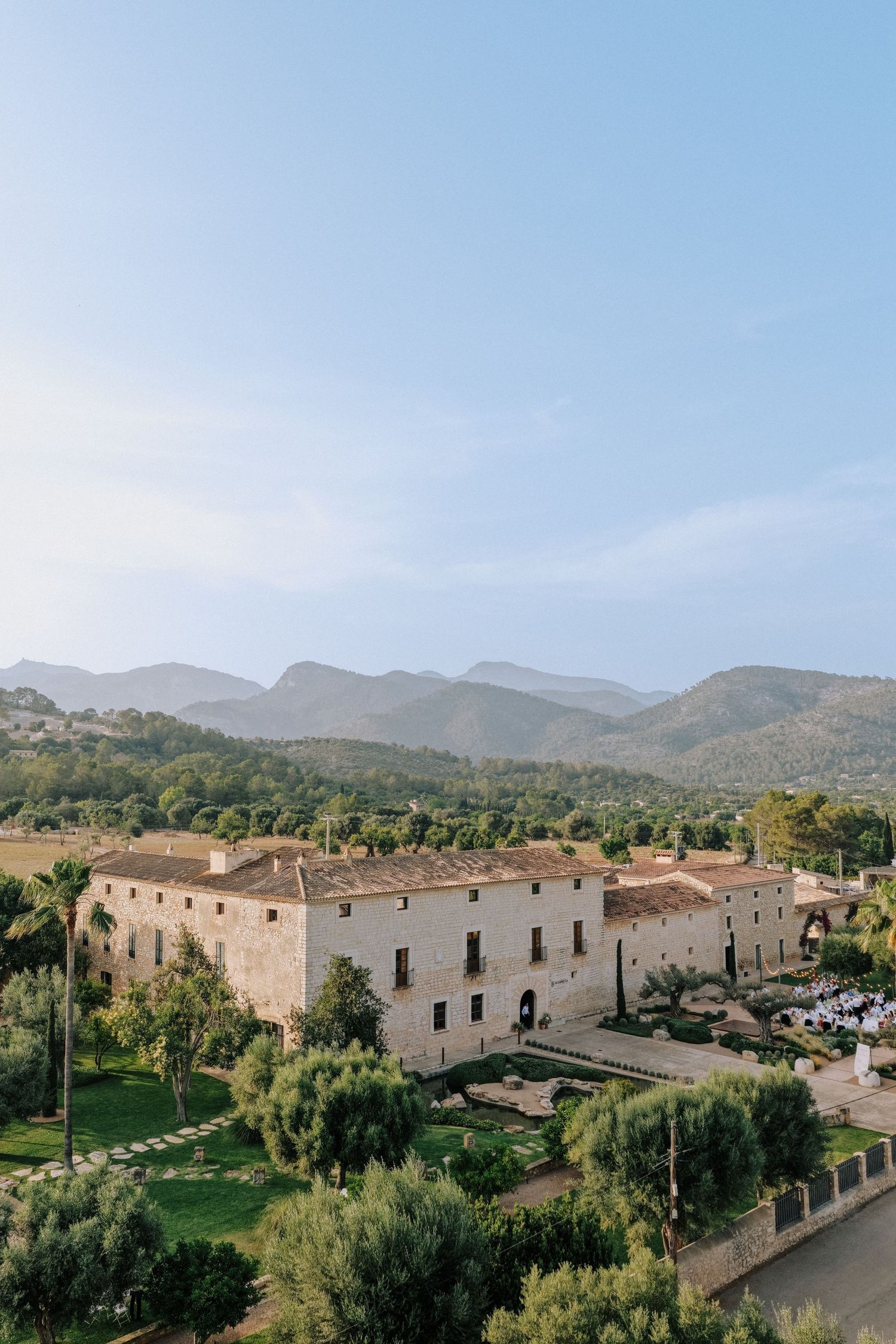 Panoramic view of a rustic stone estate nestled in mountainous countryside under blue skies.