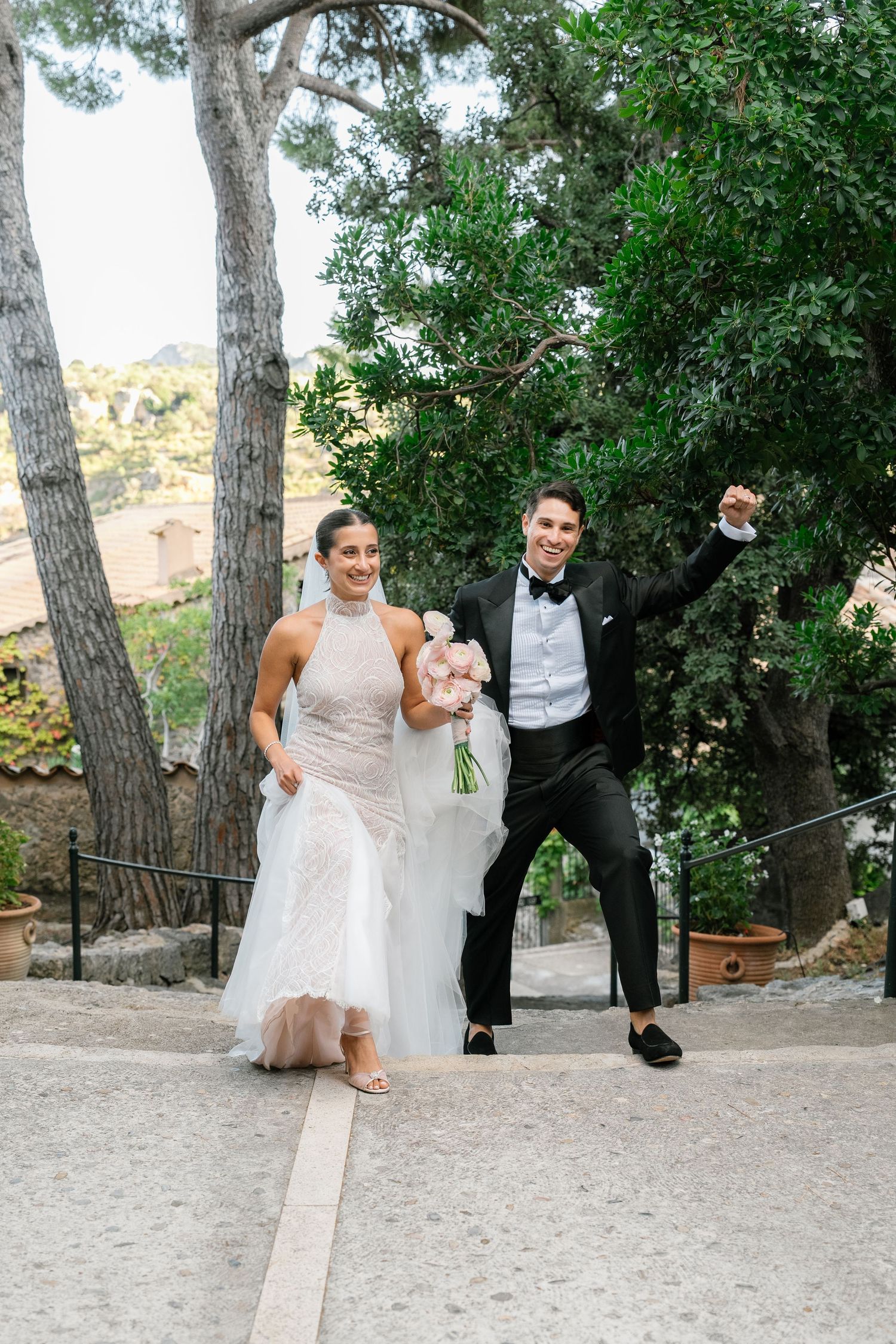 Celebratory wedding photo of couple dancing outdoors among trees.