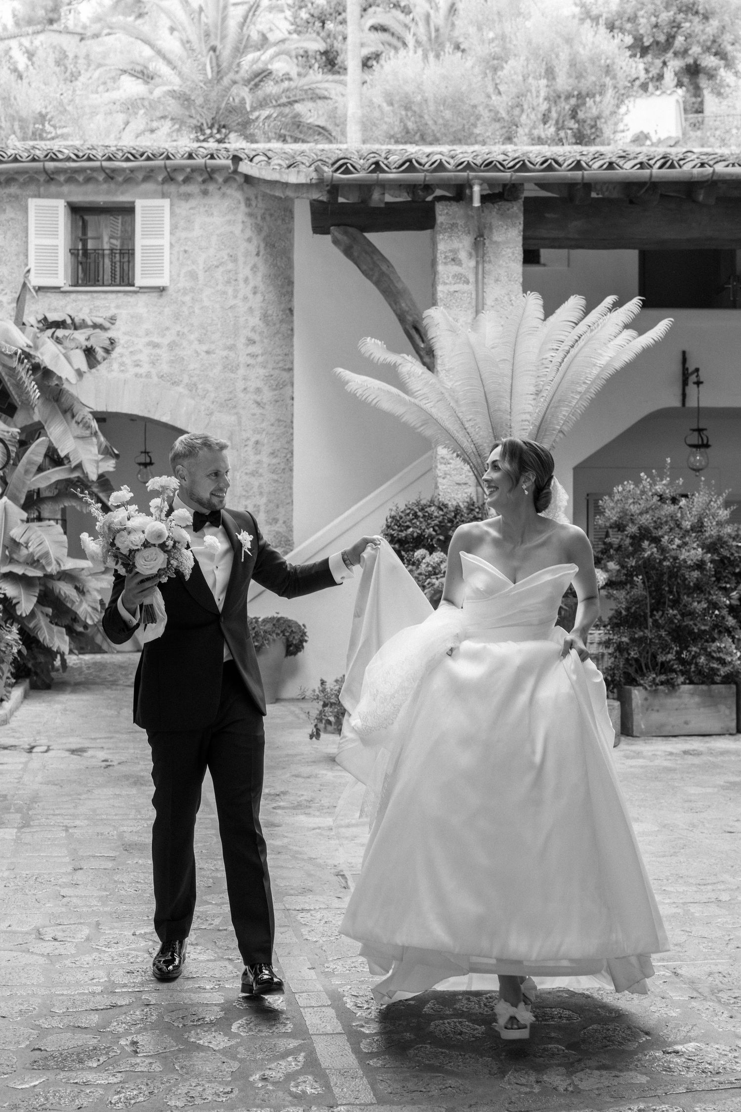 A couple dances and twirls in their wedding attire on a stone patio.