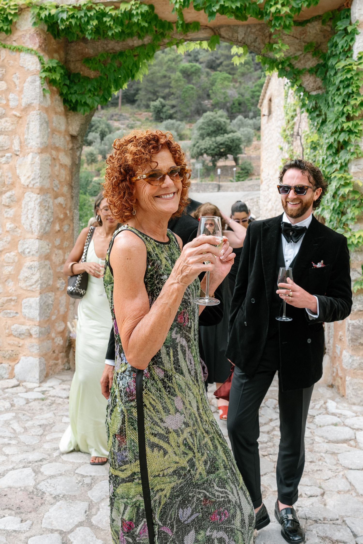 Woman with red curly hair holding champagne glass at elegant outdoor stone venue wedding reception.