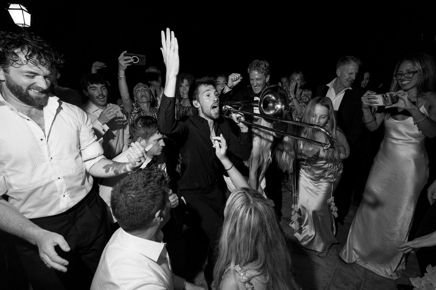 Black and white photo of a lively wedding reception with guests dancing and a band playing trombone and trumpet.