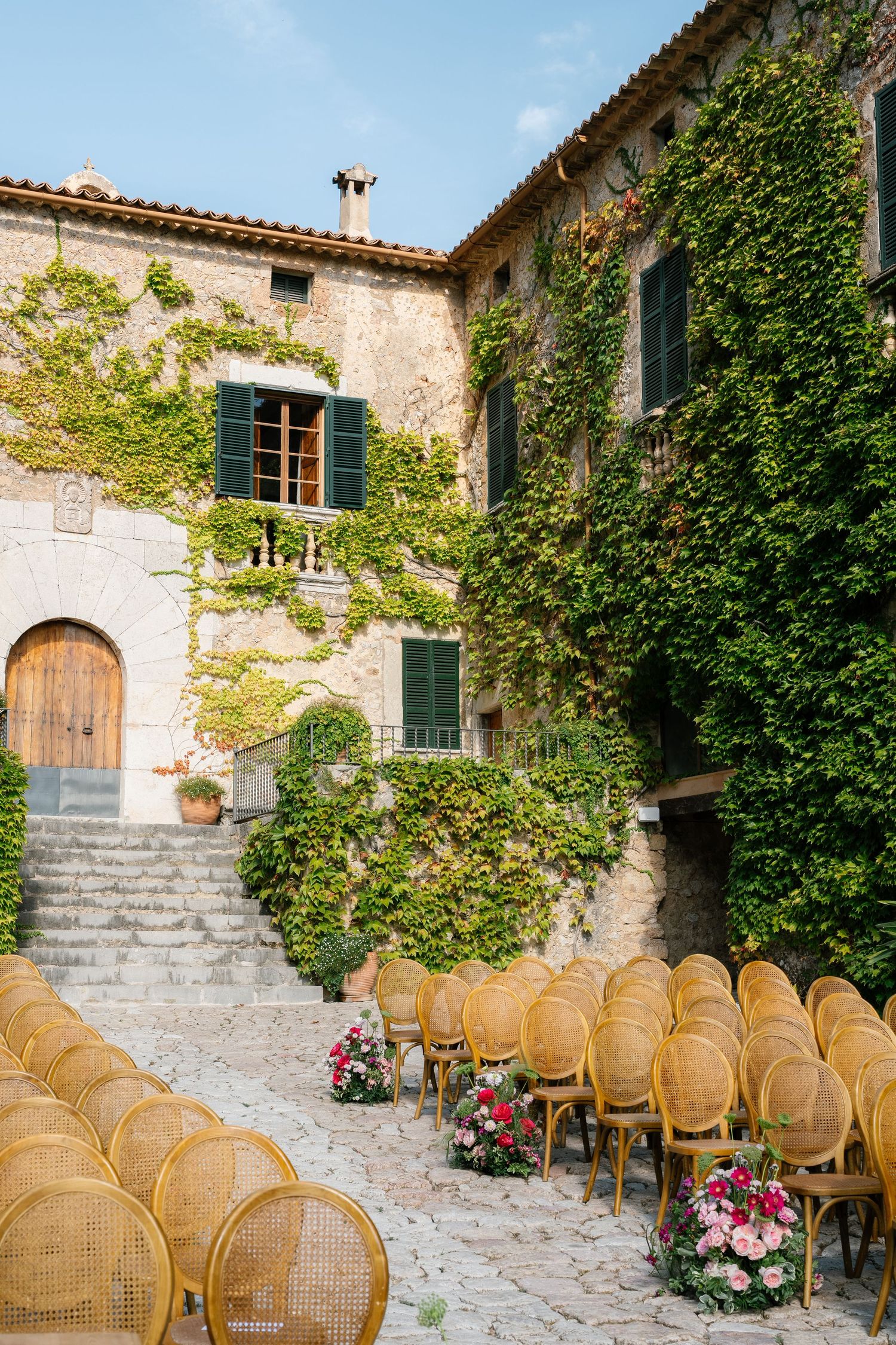 Elegant outdoor wedding venue with cane chairs arranged in rows against stone walls covered in ivy.