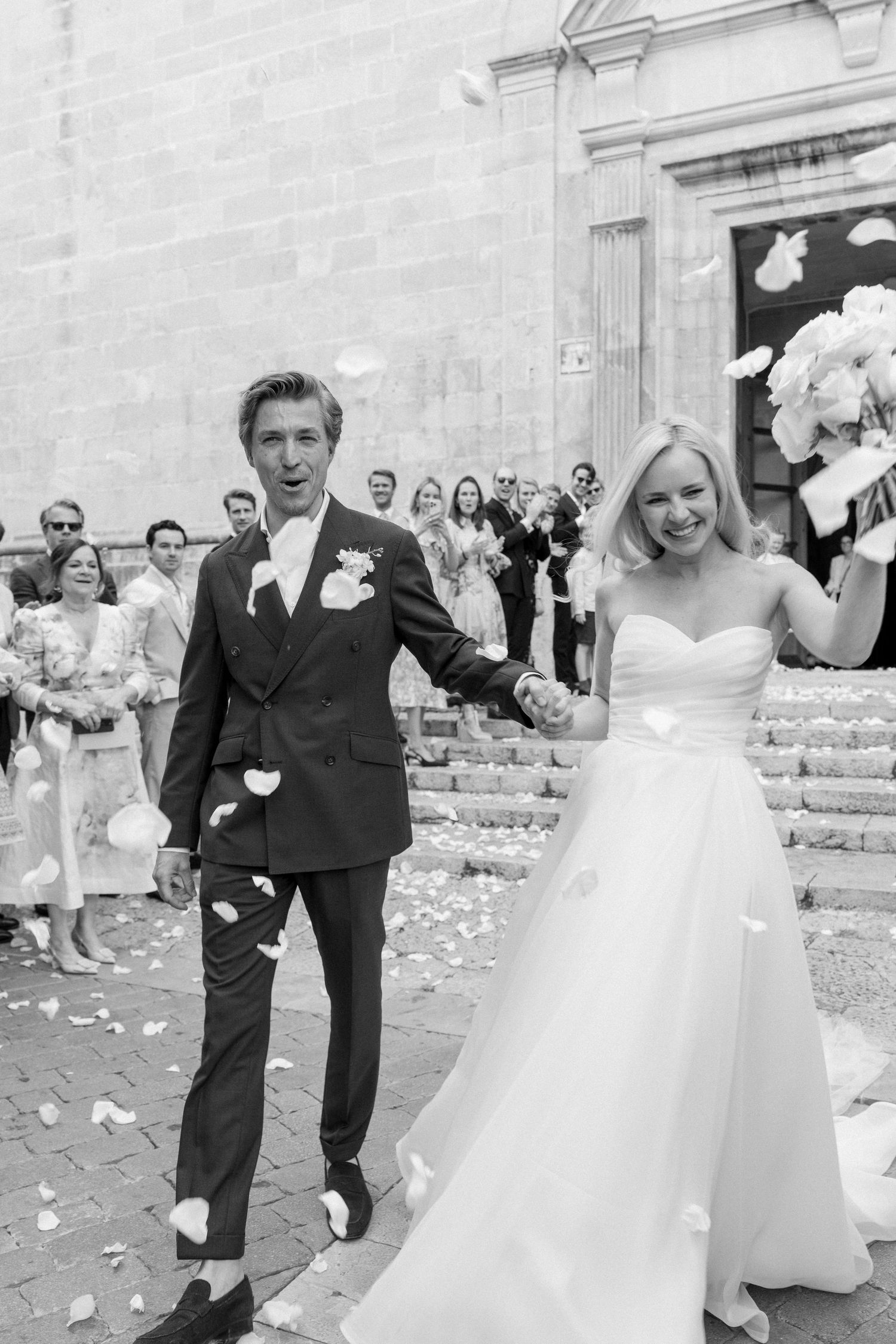 Wedding couple exiting the church as guests throw white flower petals in celebration, followed by a reception at Cal Reiet, Mallorca