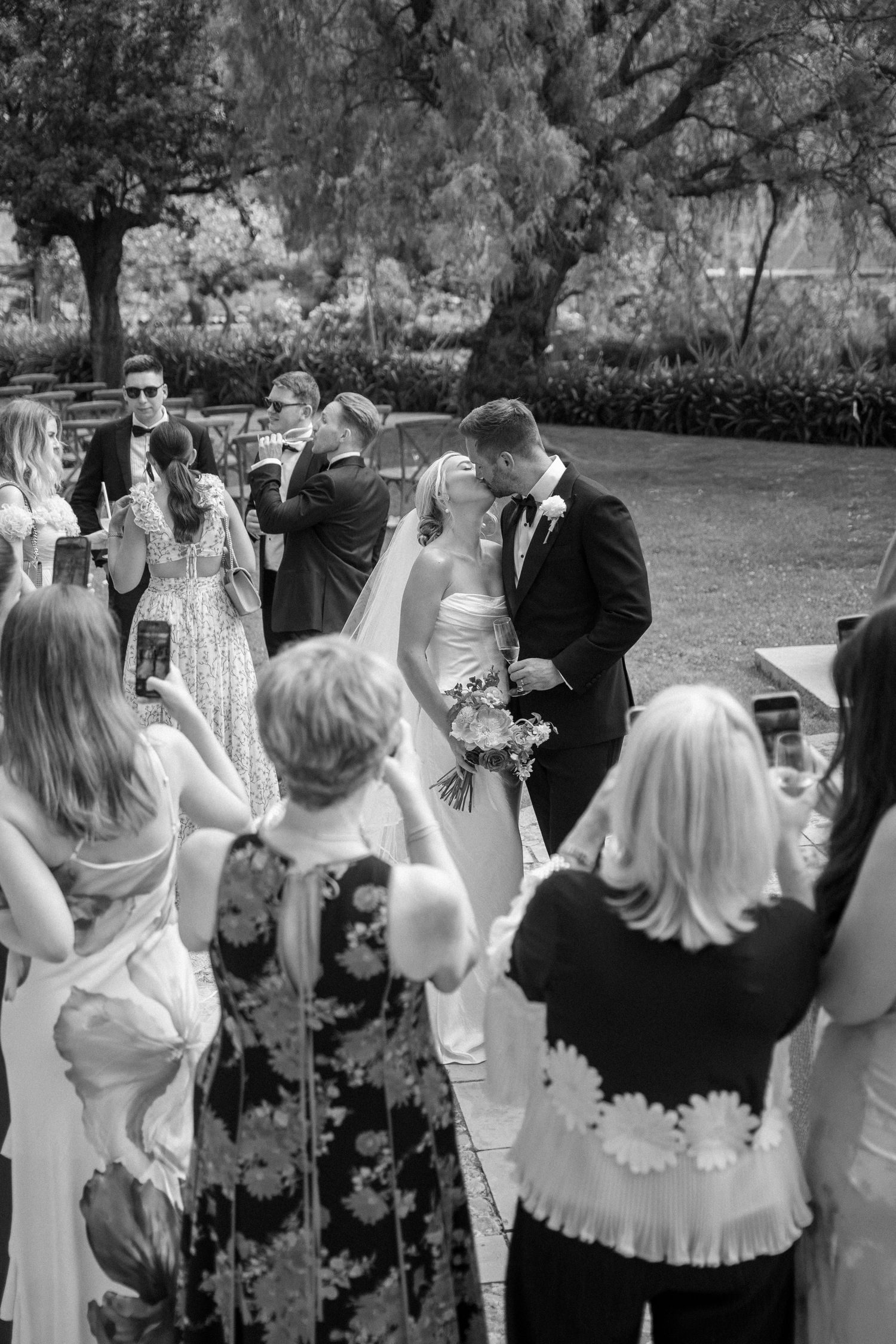 Black and white photo of wedding guests gathered in a garden setting.