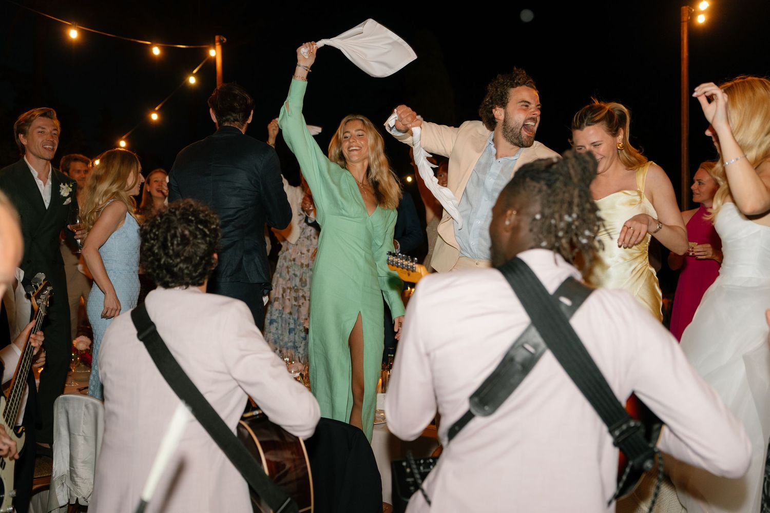 Lively dance party with guests celebrating at outdoor wedding reception under string lights.