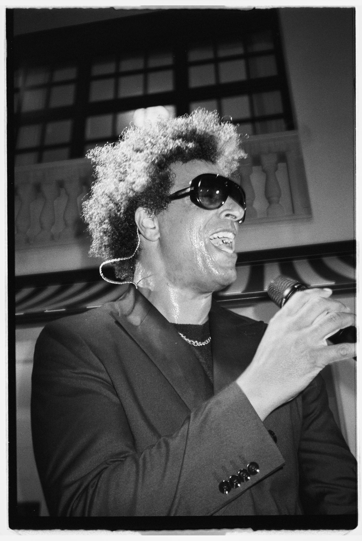 Black and white photo of a performer in sunglasses singing with enthusiasm.