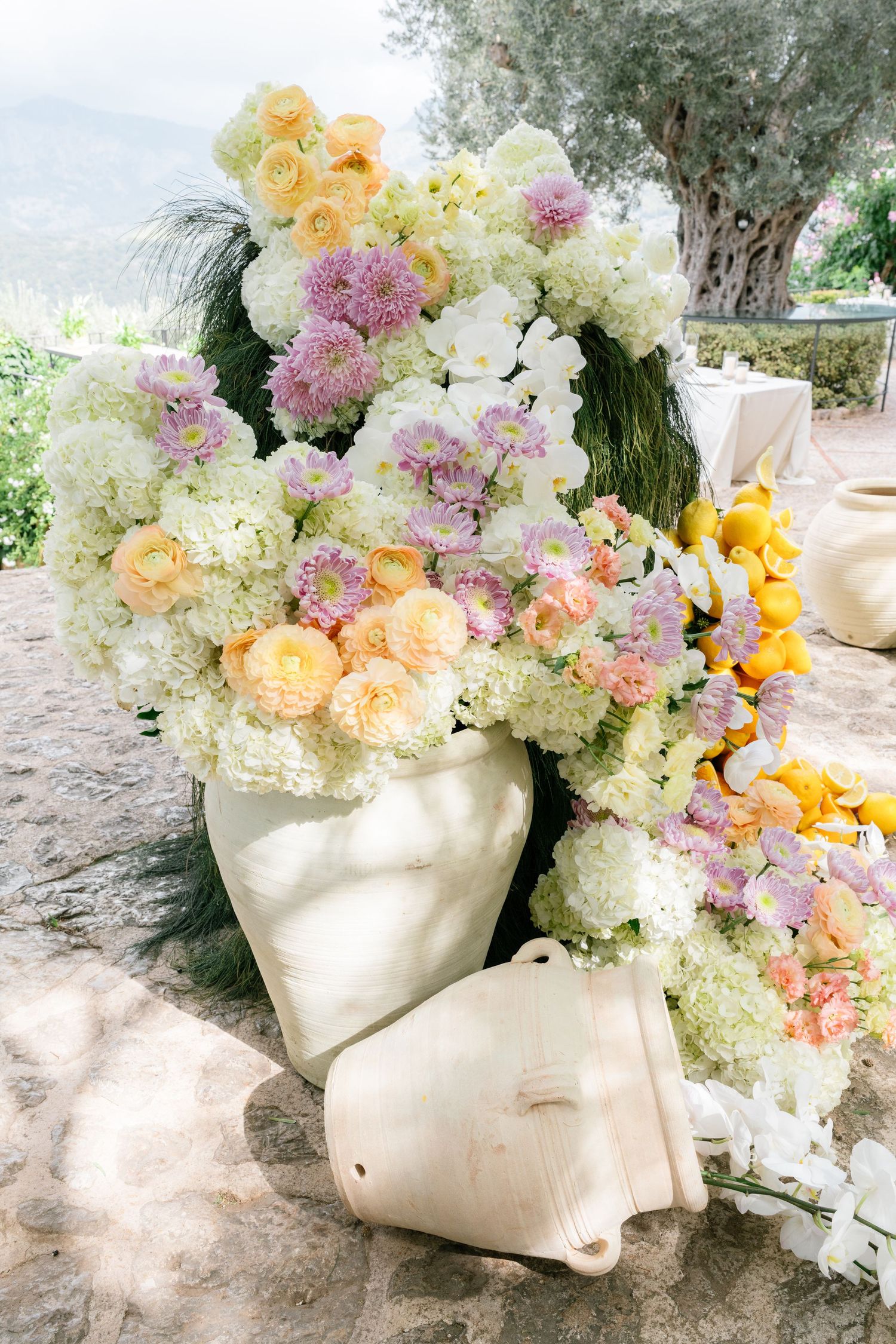 Elegant floral arrangement with white, yellow and pink blooms displayed in decorative white head-shaped vases outdoors.