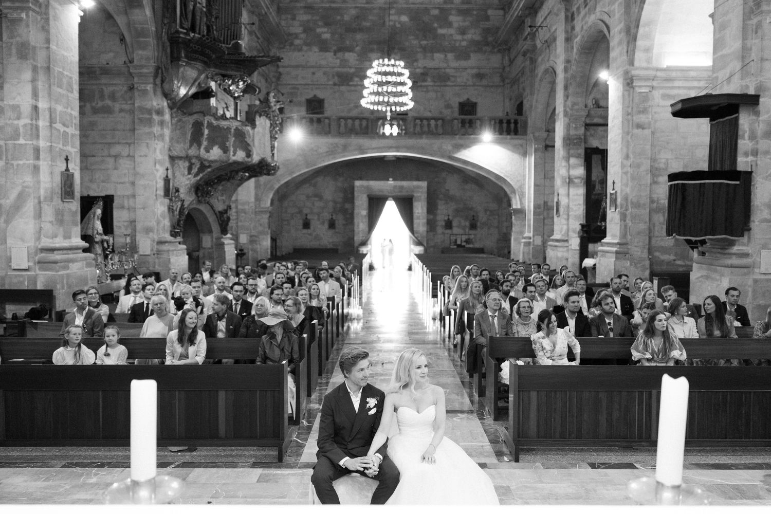 Panoramic view of a wedding ceremony in a historic stone church with guests seated in rows.