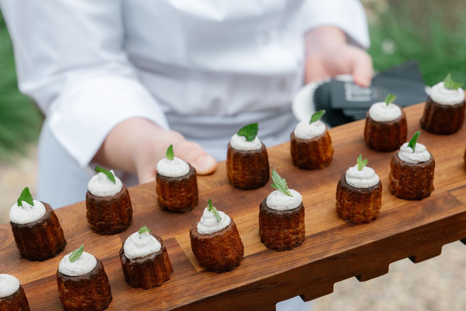 Elegant dessert display featuring miniature cakes topped with white frosting on a wooden serving board.
