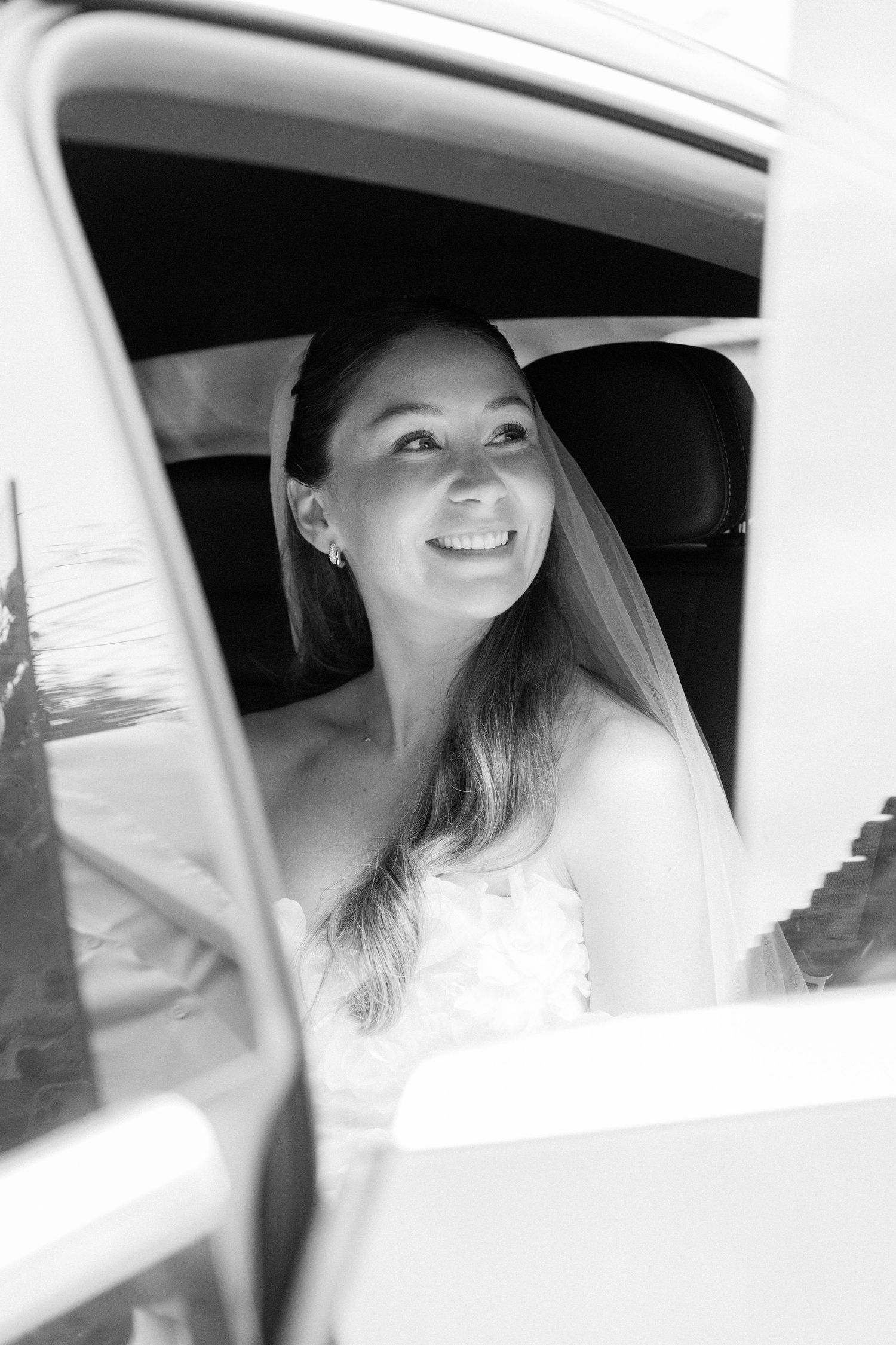 Joyful bride smiling in car window on wedding day.