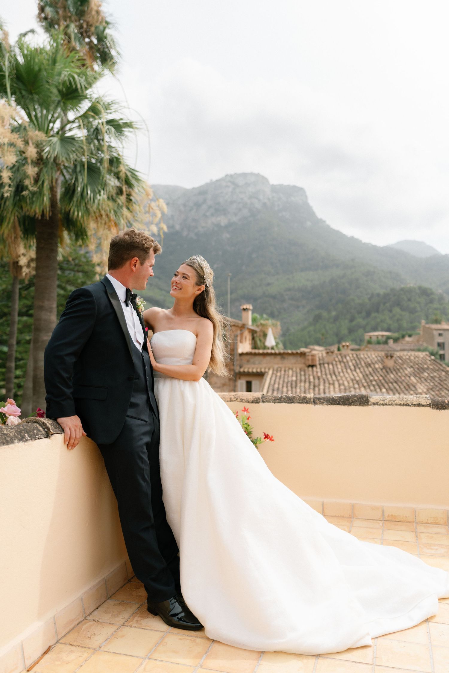 Wedding couple poses against Mediterranean landscape with mountains and palm trees.