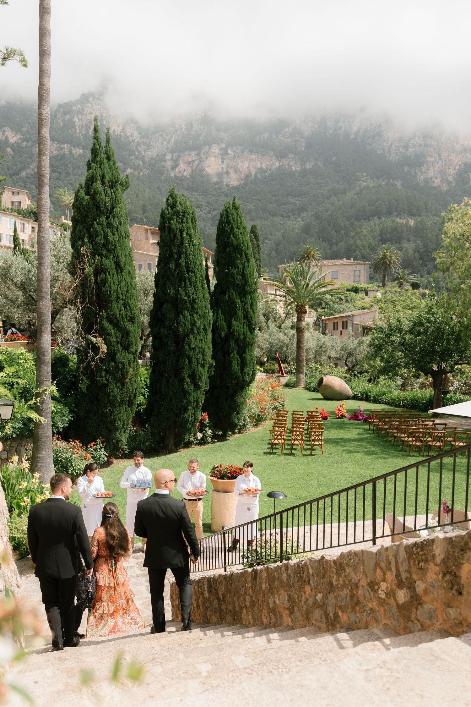 Wedding guests gather on a scenic terrace overlooking mountains and cypress trees in a Mediterranean setting.