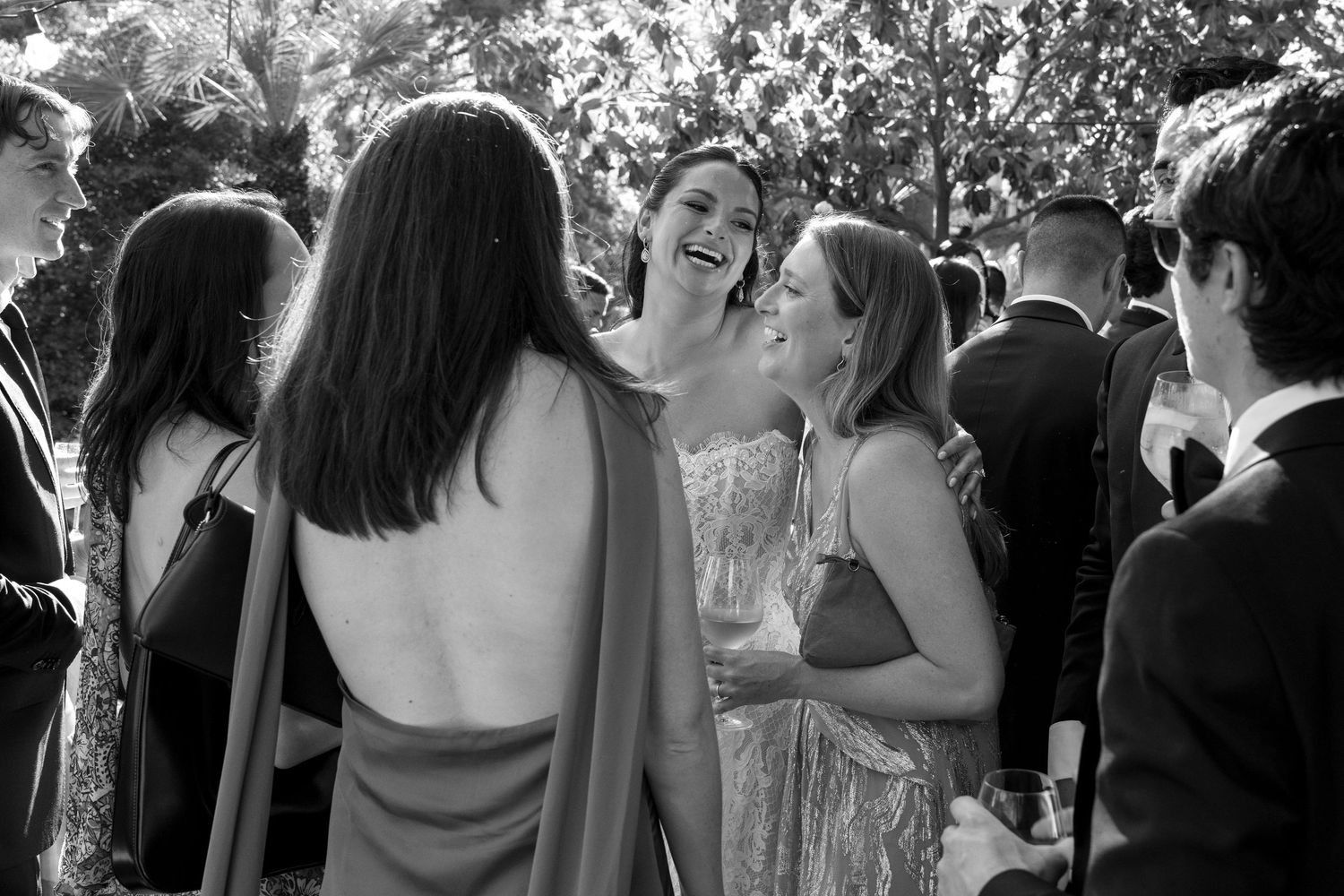 Black and white photo of elegantly dressed women laughing and socializing at a formal outdoor event.