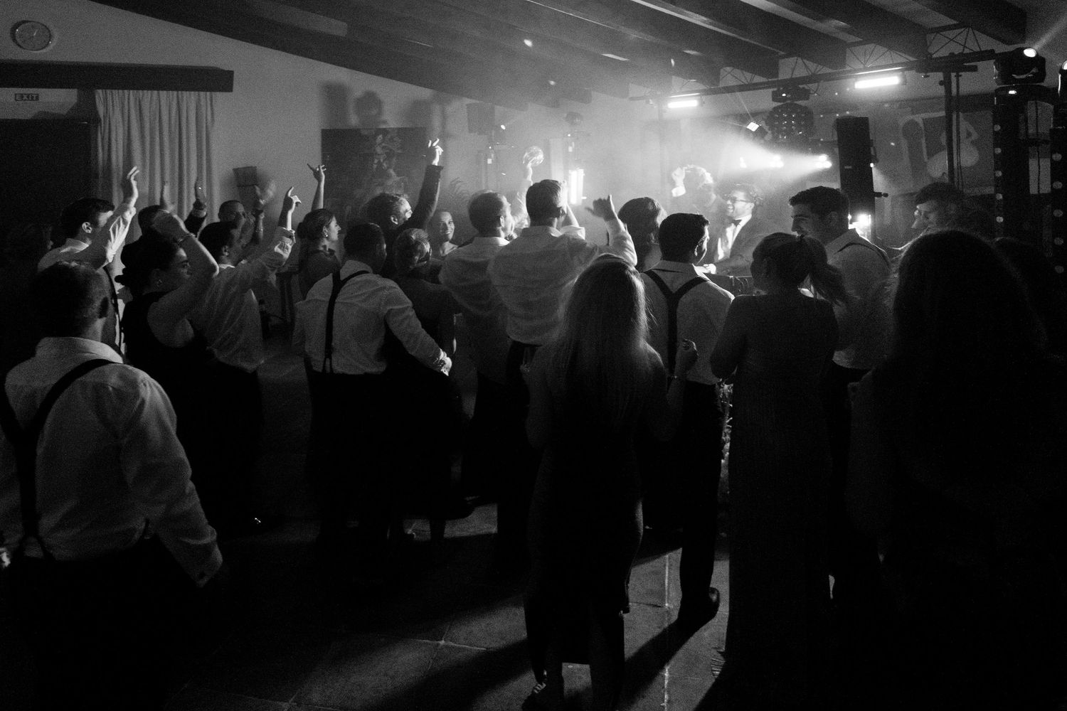 Silhouettes of wedding guests dancing in a dimly lit reception venue with atmospheric lighting.