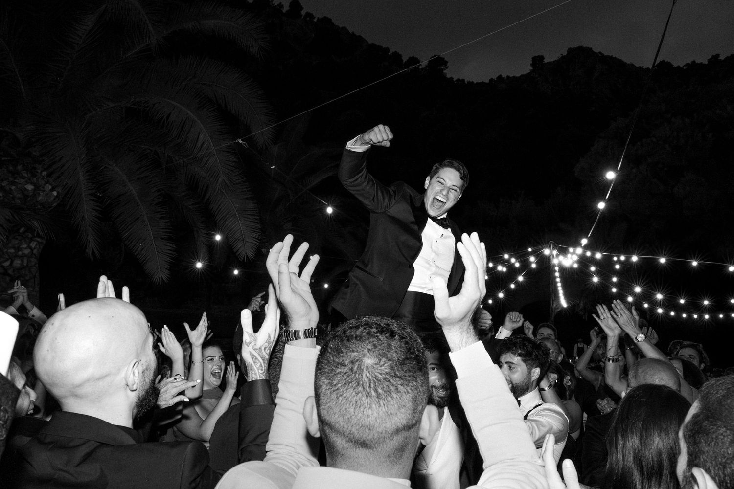 Dark reception venue with silhouettes of guests dancing under string lights.