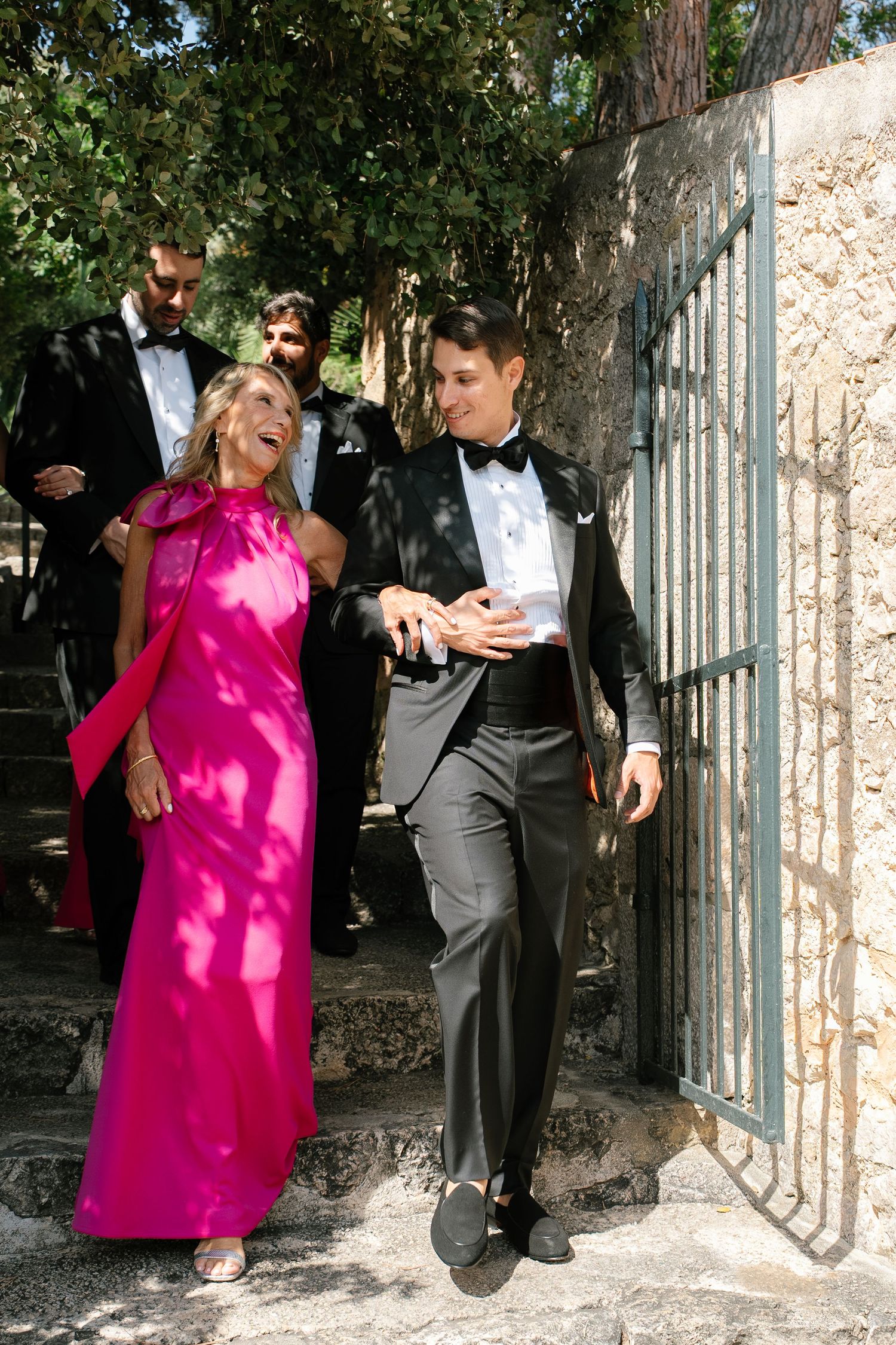 Wedding party members walk together with one wearing a vibrant pink dress outdoors.
