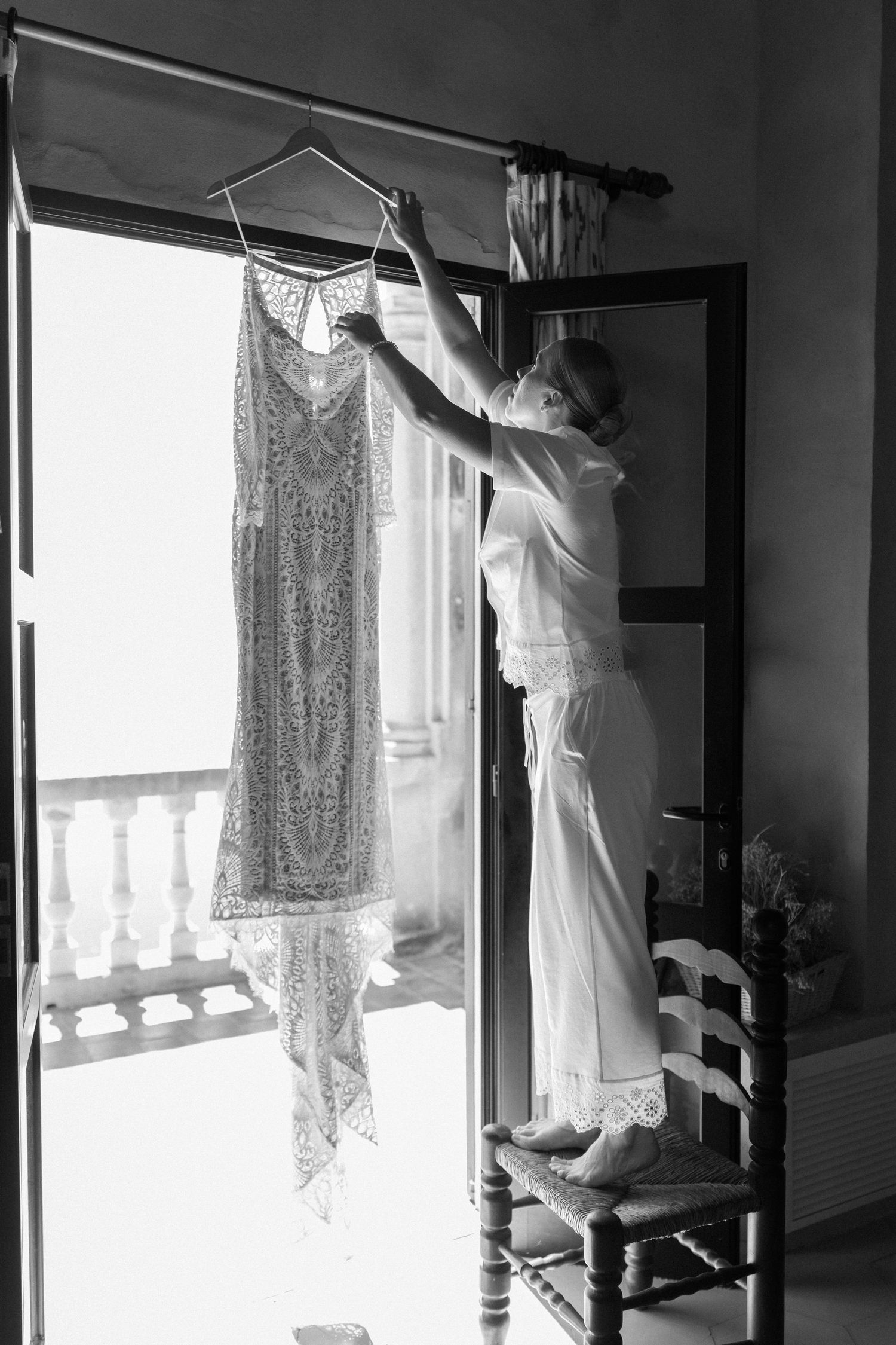 Delicate white wedding dress being photographed against a bright window in black and white.
