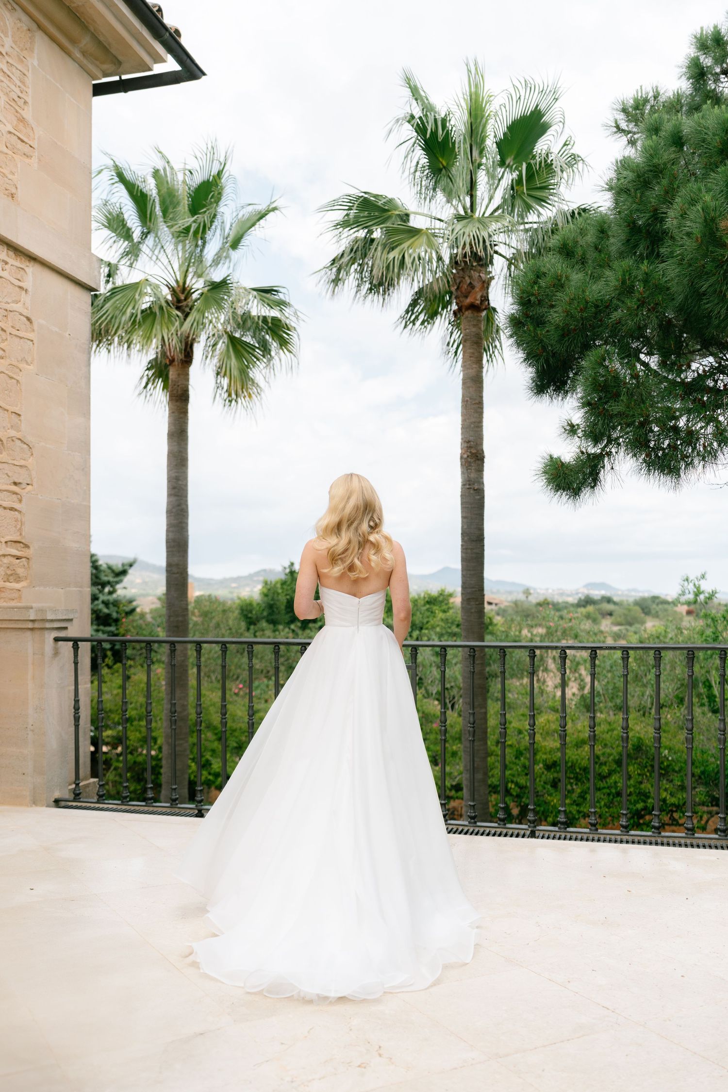 Elegant white wedding dress photographed on a terrace with palm trees and scenic views.