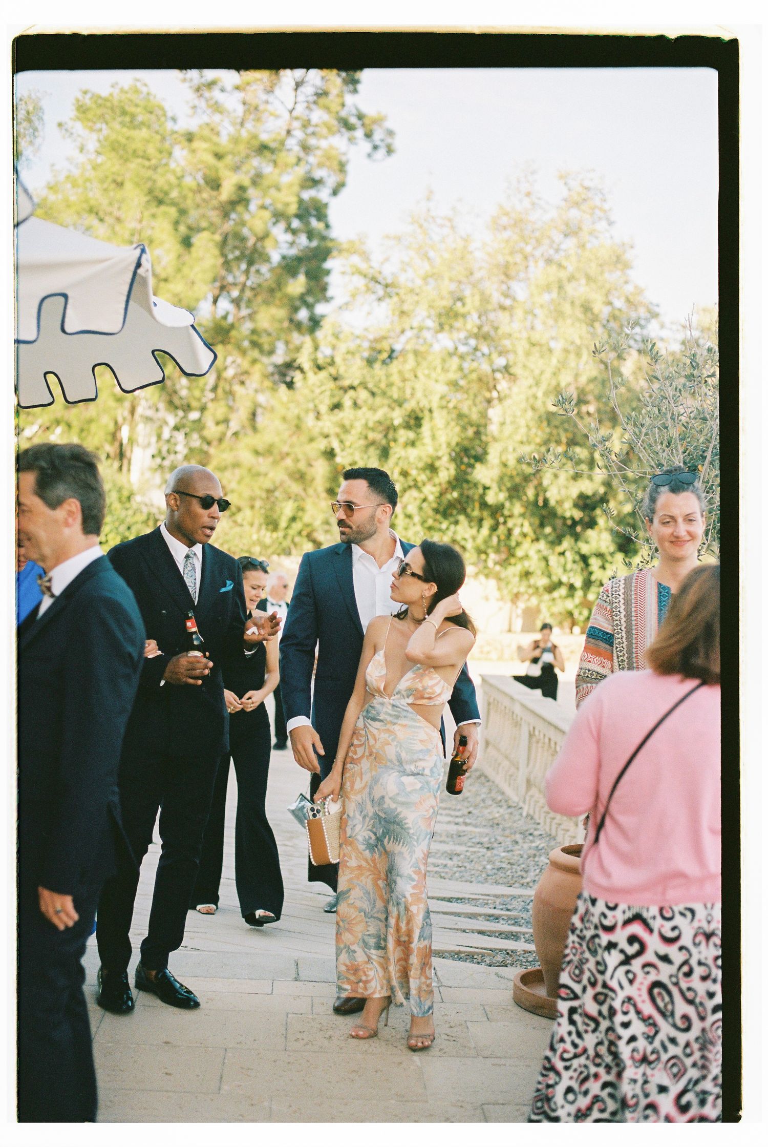Wedding guests in formal attire mingle during an outdoor reception on a stone patio.