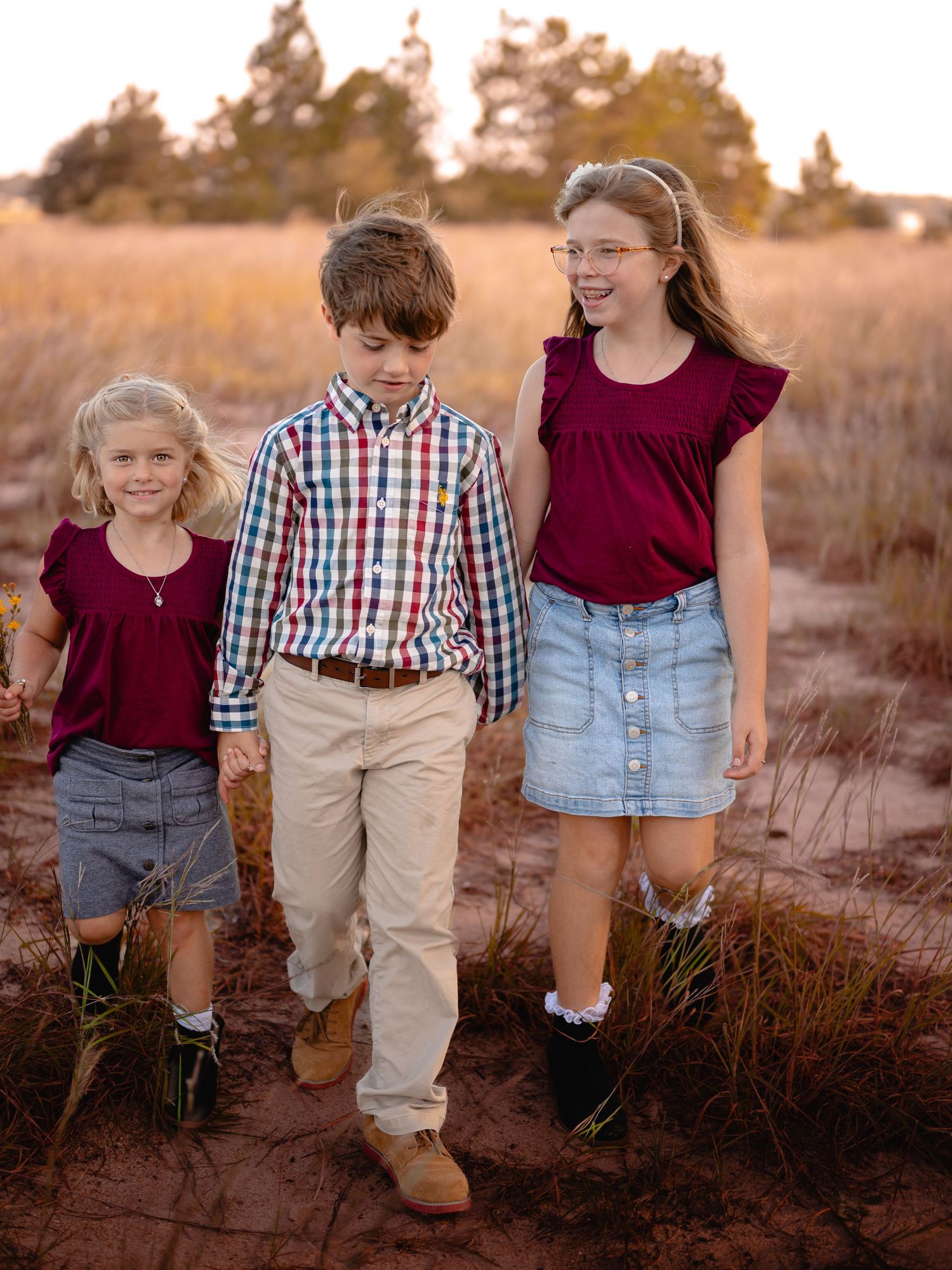 Siblings walking together in a golden field at sunset. Candid family photo by Photography by Kylee Mason, located in Chesapeake VA.