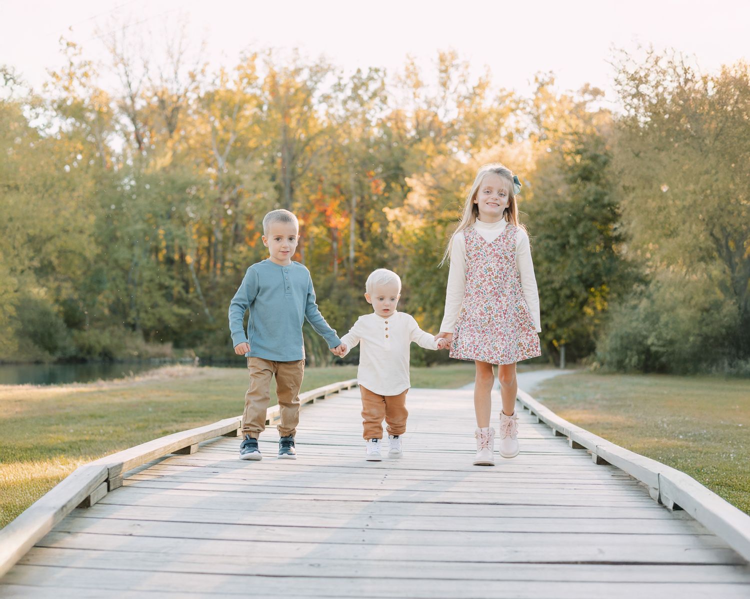 two young kids all holding hands with baby in the middle walking across a bridge in Fishers, IN