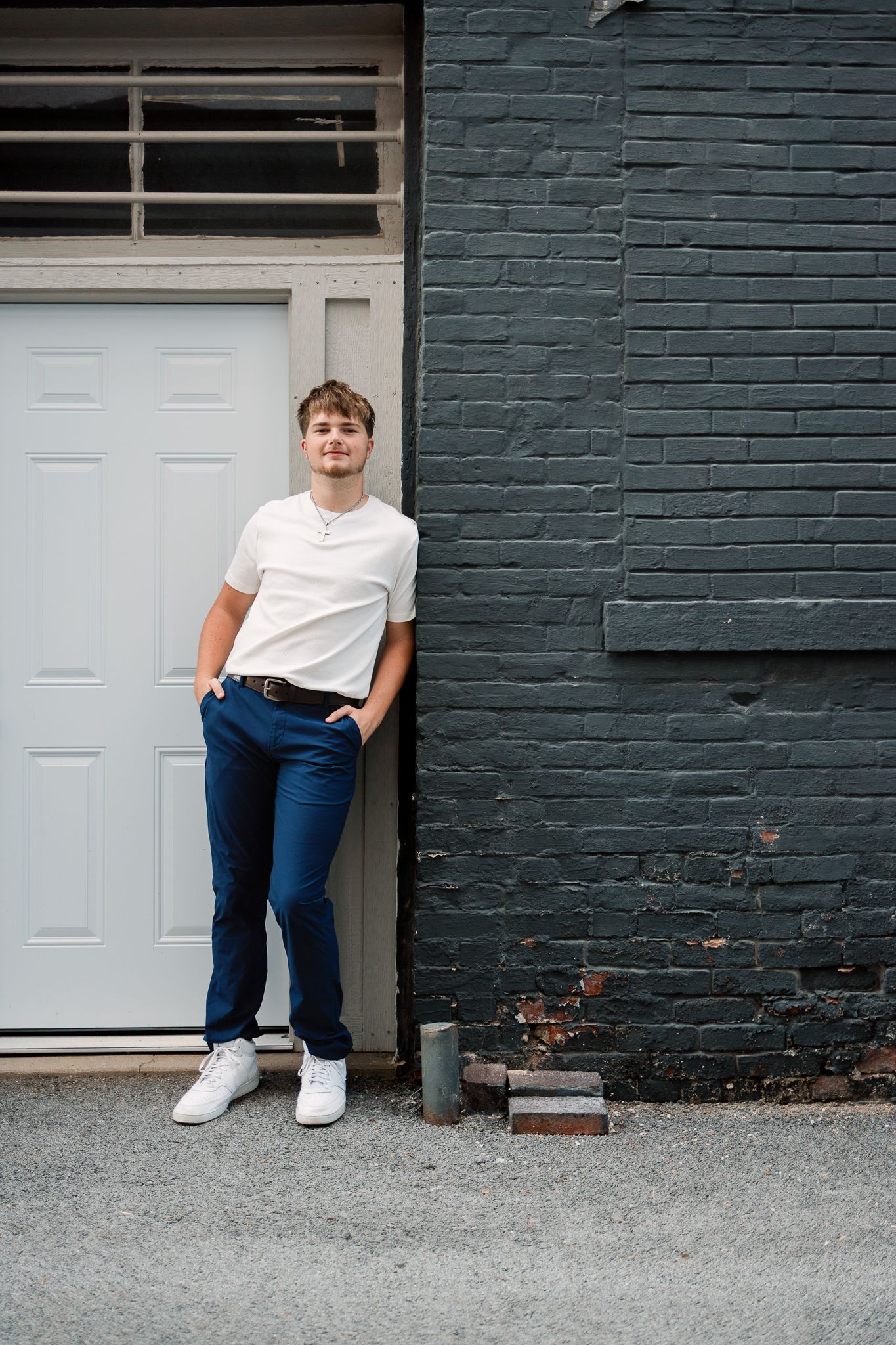 senior leaning on against a white door and dark gray brick wall